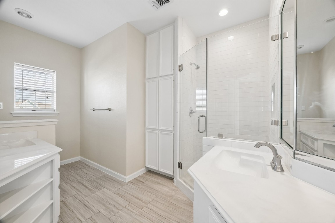 This modern bathroom features a sleek glass-enclosed shower, white cabinetry, and contemporary fixtures. The space is bright and airy, with pale tile flooring and a neutral color palette, providing a clean and inviting atmosphere.