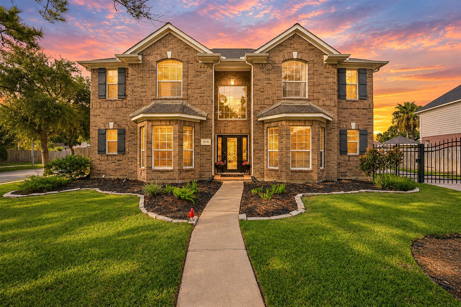 Stately two-story brick home with elegant bay windows, manicured landscaping, and a welcoming pathway leading to the front entrance.
