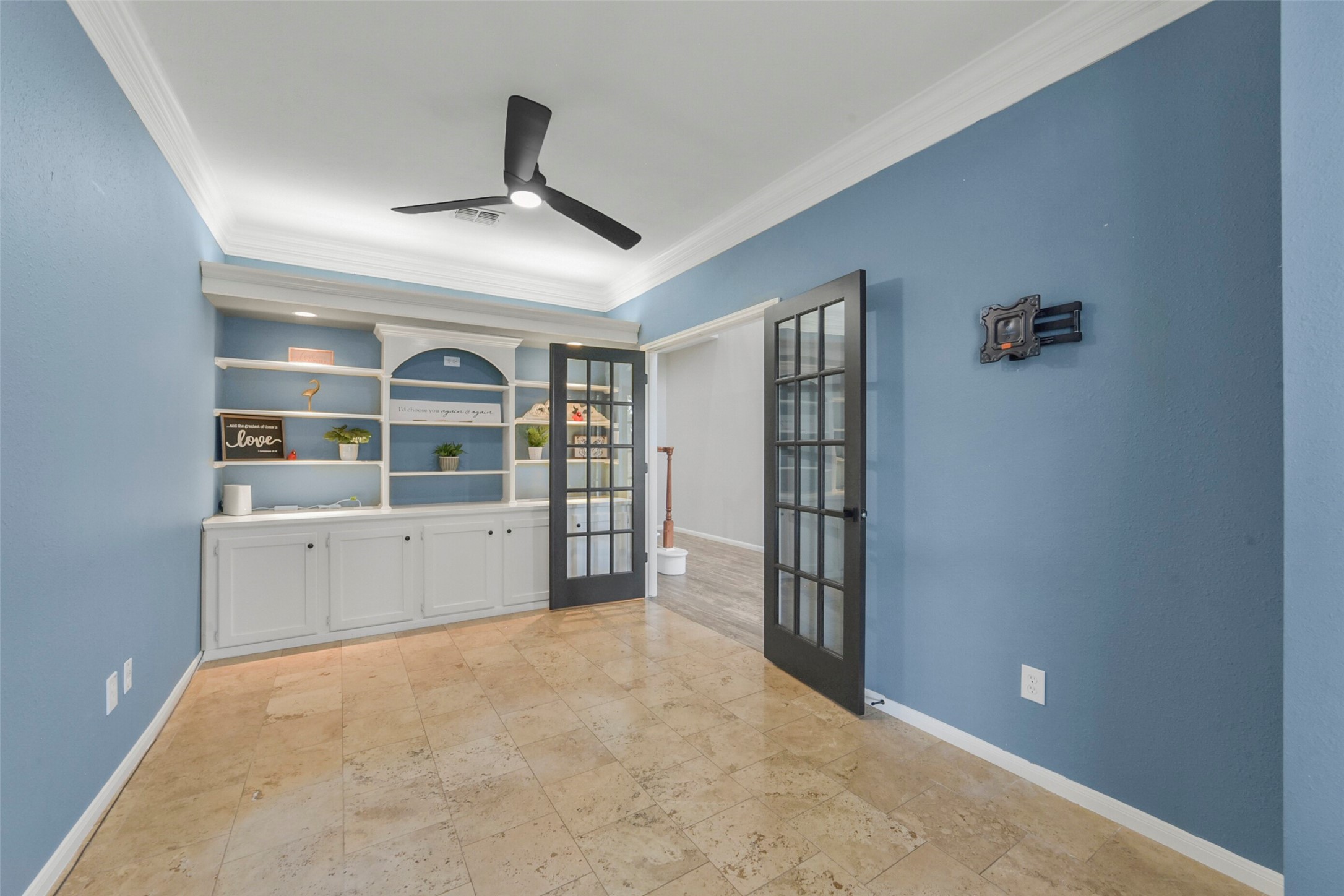 Elegant office featuring a built-in shelving unit, stylish French doors, and a modern ceiling fan, all set against soothing blue walls.