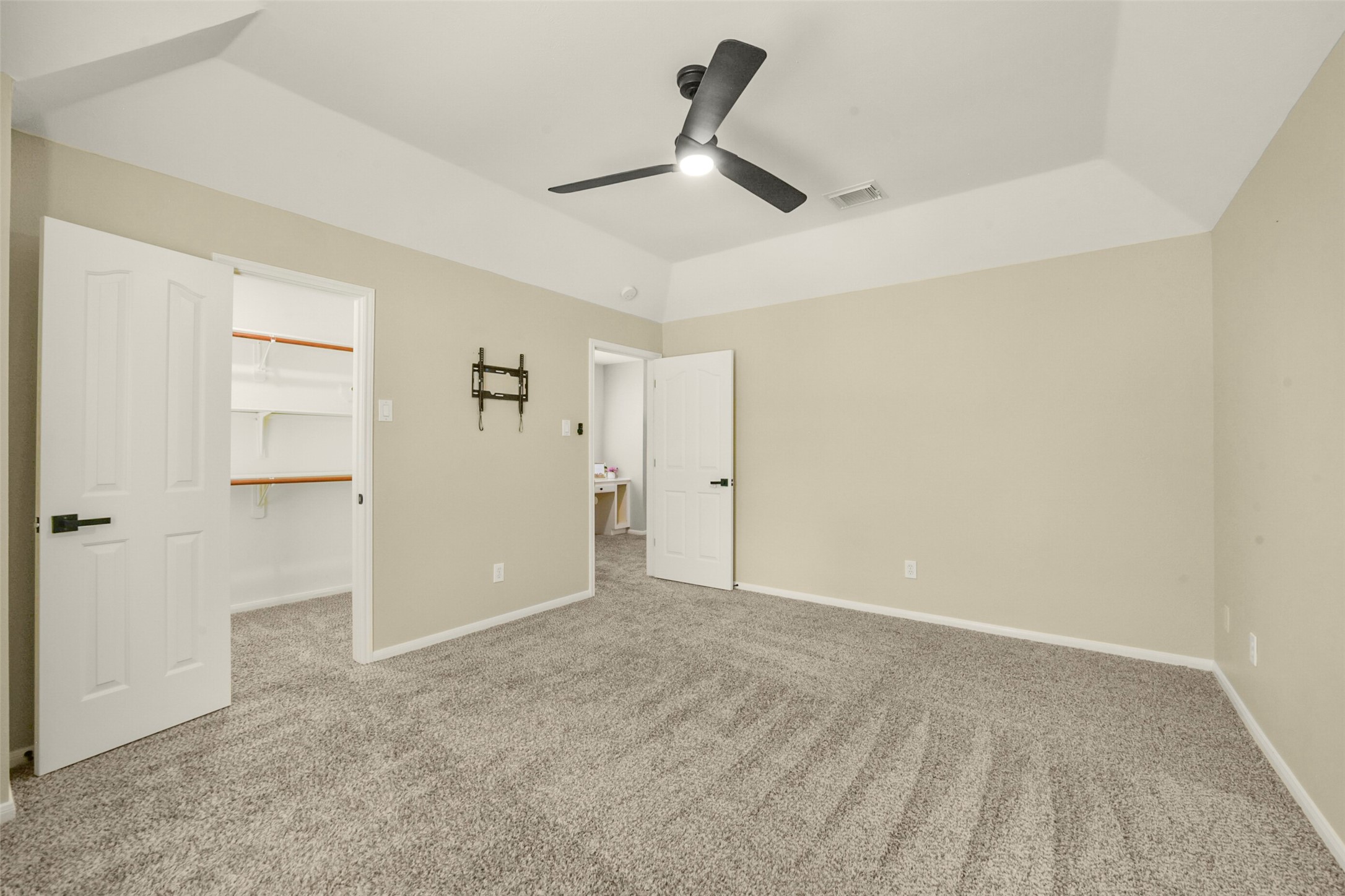Spacious bedroom featuring plush carpet, a ceiling fan, and ample natural light, with convenient access to a walk-in closet.