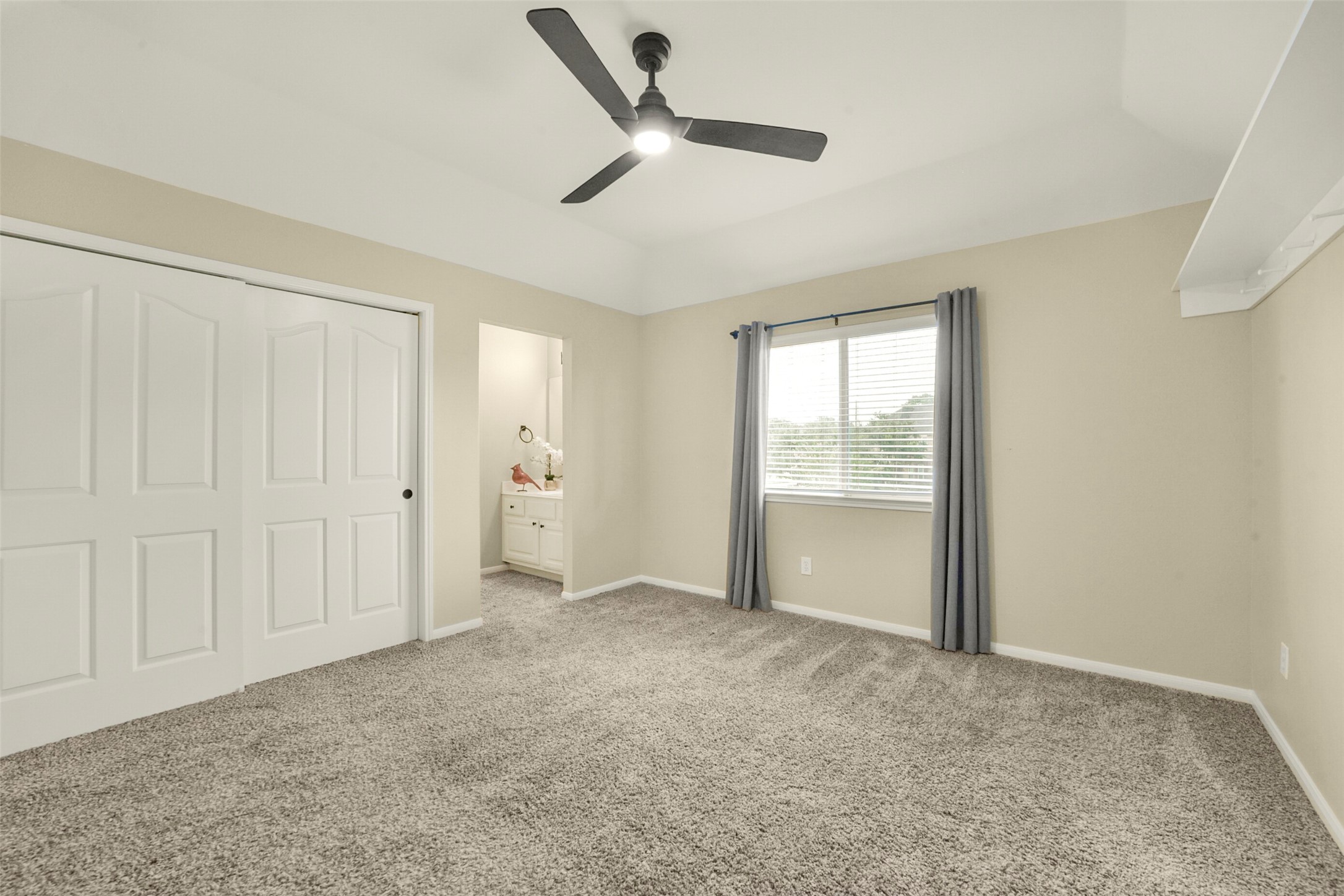 Spacious bedroom with plush carpeting, a modern ceiling fan, and ample natural light from a large window. Includes a convenient Jack and Jill bathroom and a double-door closet for ample storage.