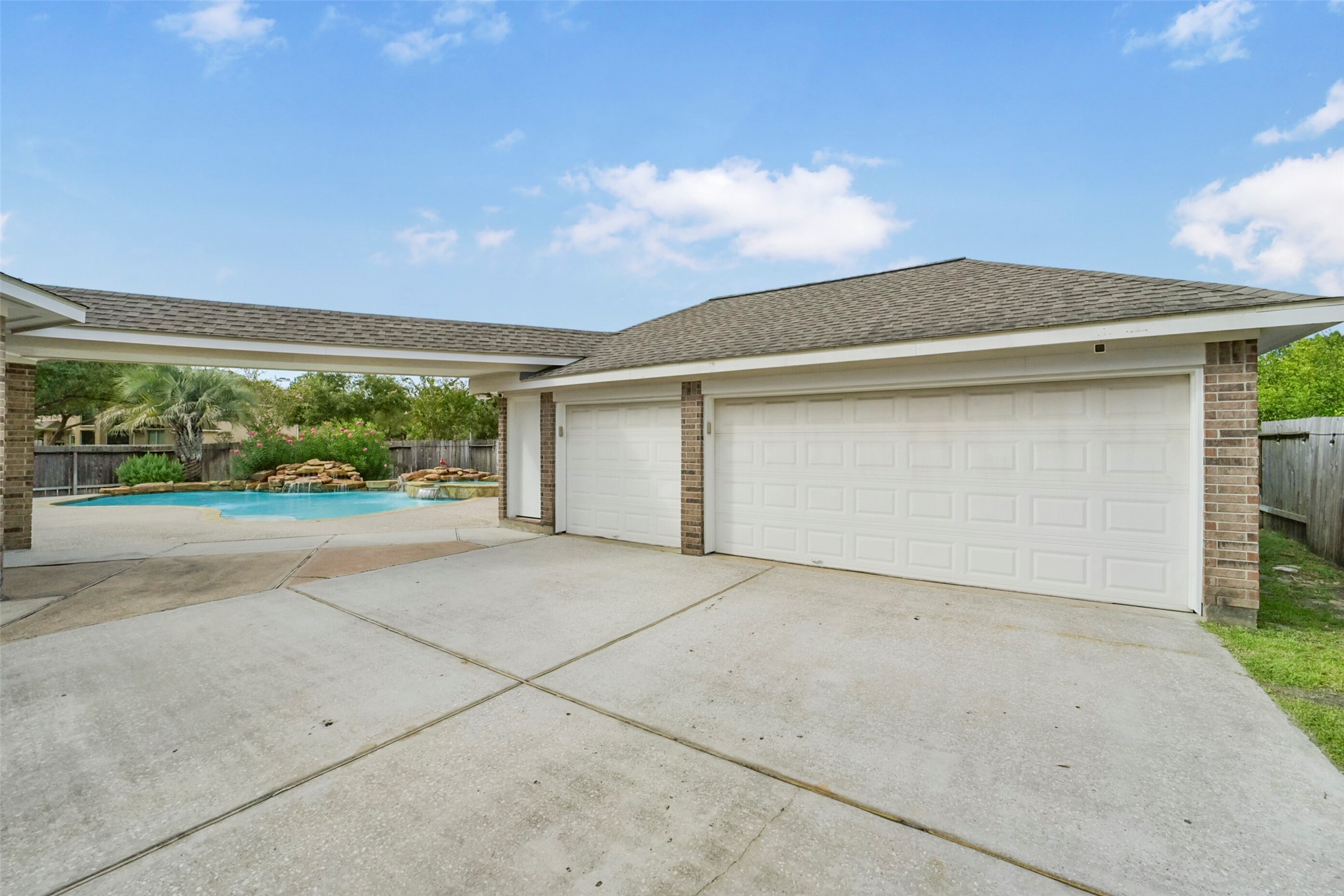 Spacious driveway leads to a large three-car garage, with a glimpse of a refreshing backyard pool area perfect for relaxation.