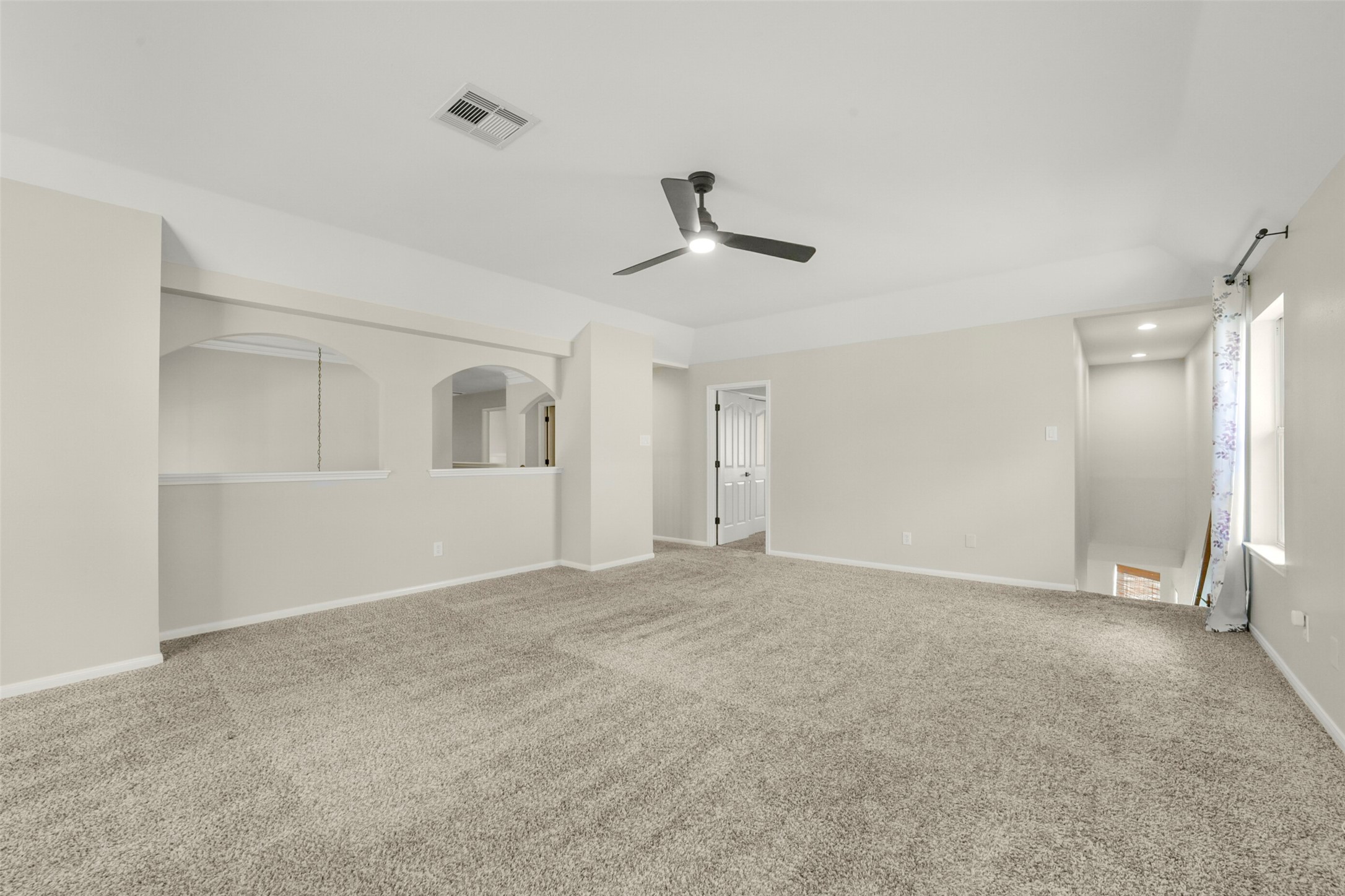Spacious living area with plush carpeting, neutral tones, and a ceiling fan, offering a cozy and inviting atmosphere.