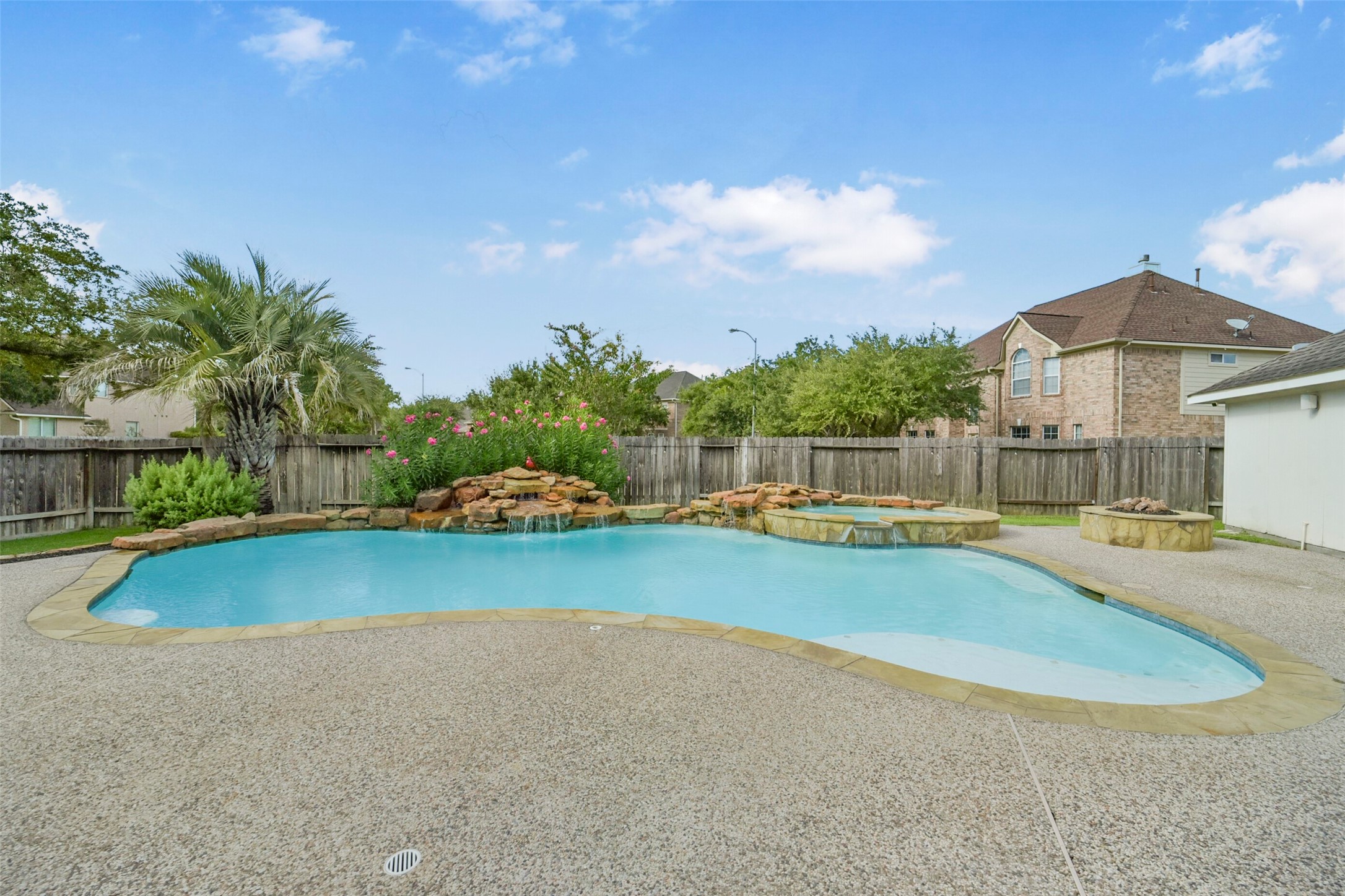 Enjoy a private oasis with this stunning backyard featuring a sparkling pool, soothing waterfall, and a cozy fire pit, all surrounded by lush greenery for ultimate relaxation.
