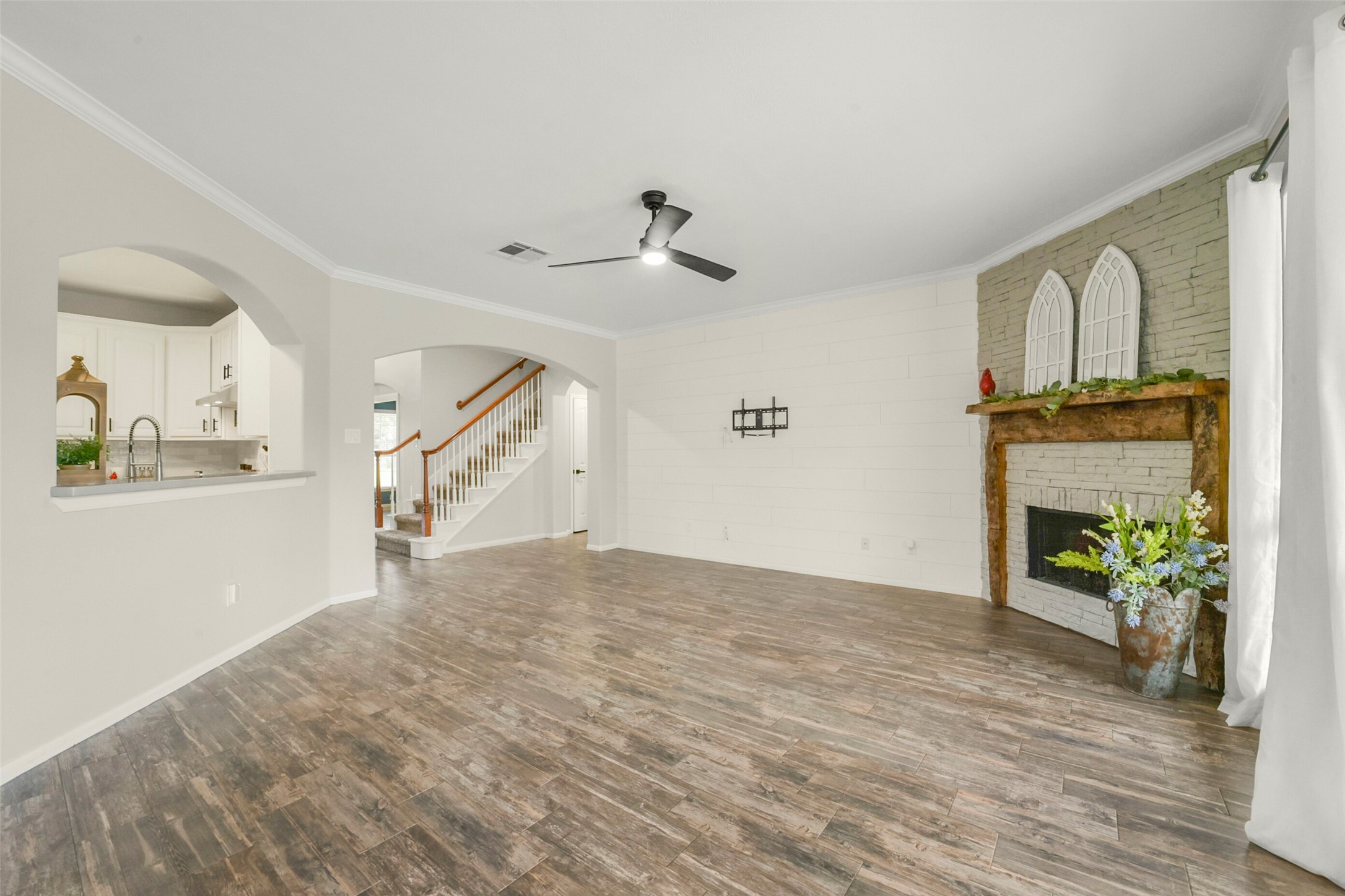 Spacious living area with elegant wood flooring, a charming brick fireplace, and abundant natural light from large windows overlooking the backyard.
