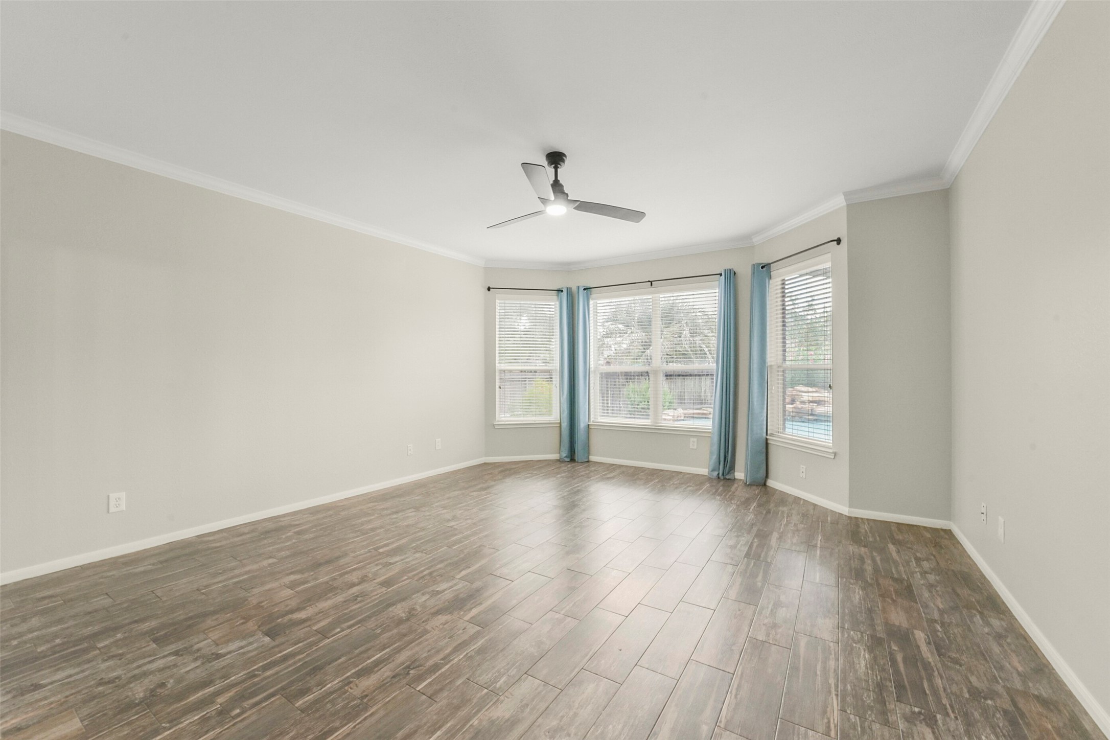 Spacious primary bedroom with elegant wood-look tile flooring, abundant natural light from large windows, and a sleek ceiling fan for comfort.