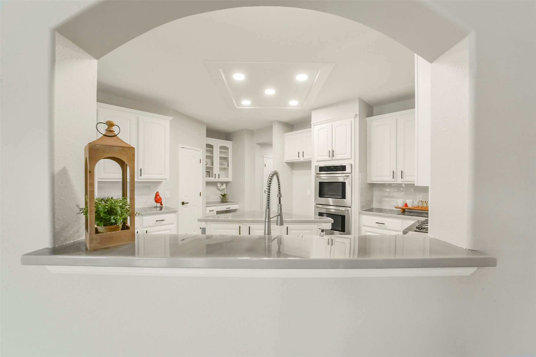 Elegant kitchen featuring modern stainless steel appliances, pristine white cabinetry, and a sleek arched pass-through for effortless entertaining.