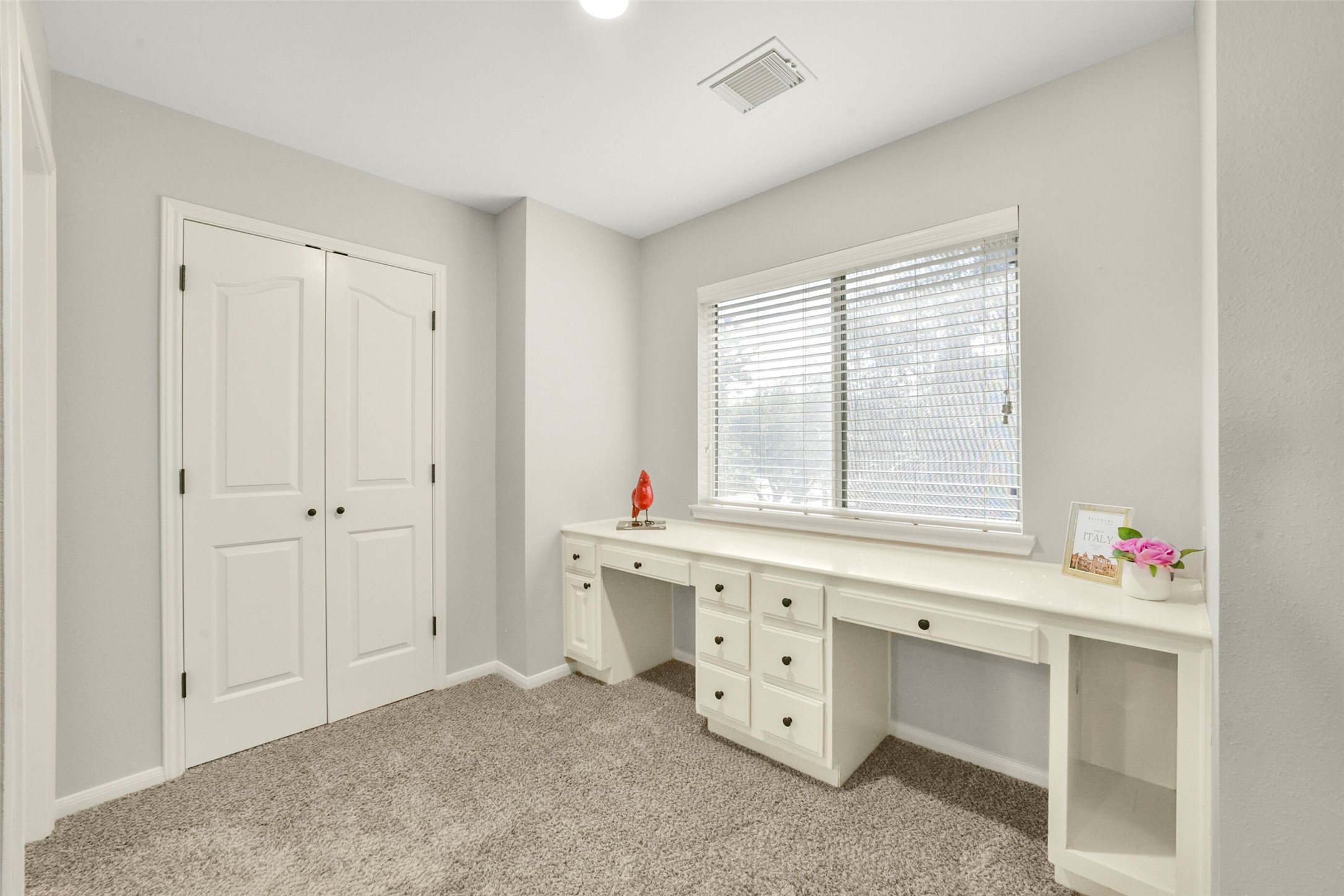 Bright and inviting workspace featuring a built-in desk with ample storage, plush carpeting, and a large window for natural light.