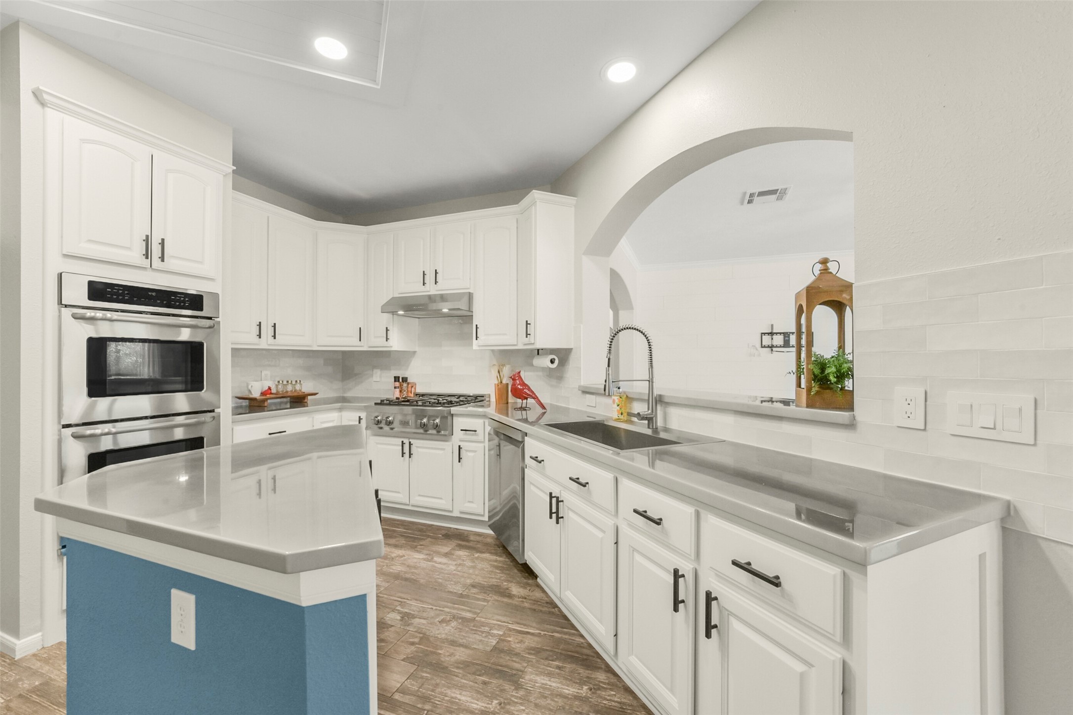 Bright and spacious kitchen featuring sleek stainless steel appliances, elegant white cabinetry, and a large island with ample counter space, all complemented by stylish wood flooring and recessed lighting.