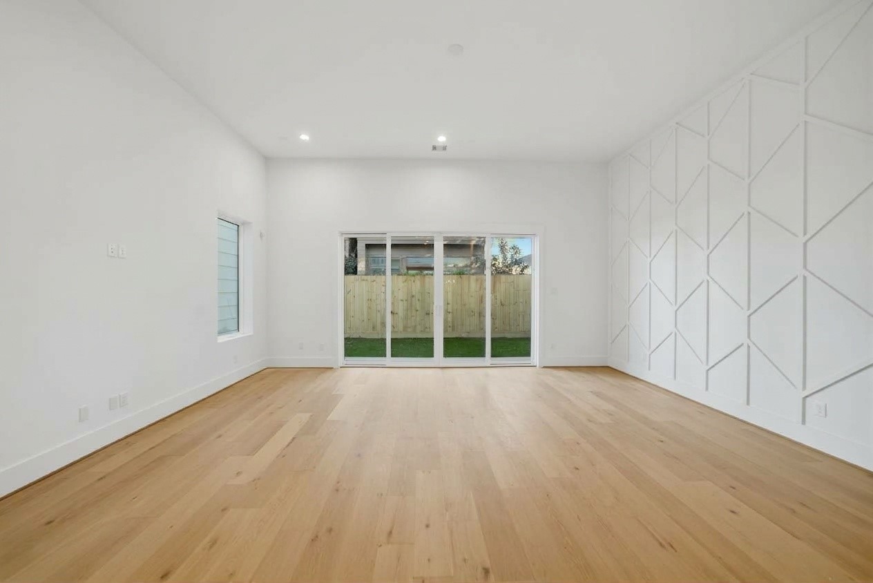 Featuring soaring ceilings, light modern hardwood floors, and a striking geometric feature wall, this bright open-concept living space is perfect for modern living. Large wall-to-wall sliding glass doors flood the room with natural light and open directly to a private, fully fenced backyard area