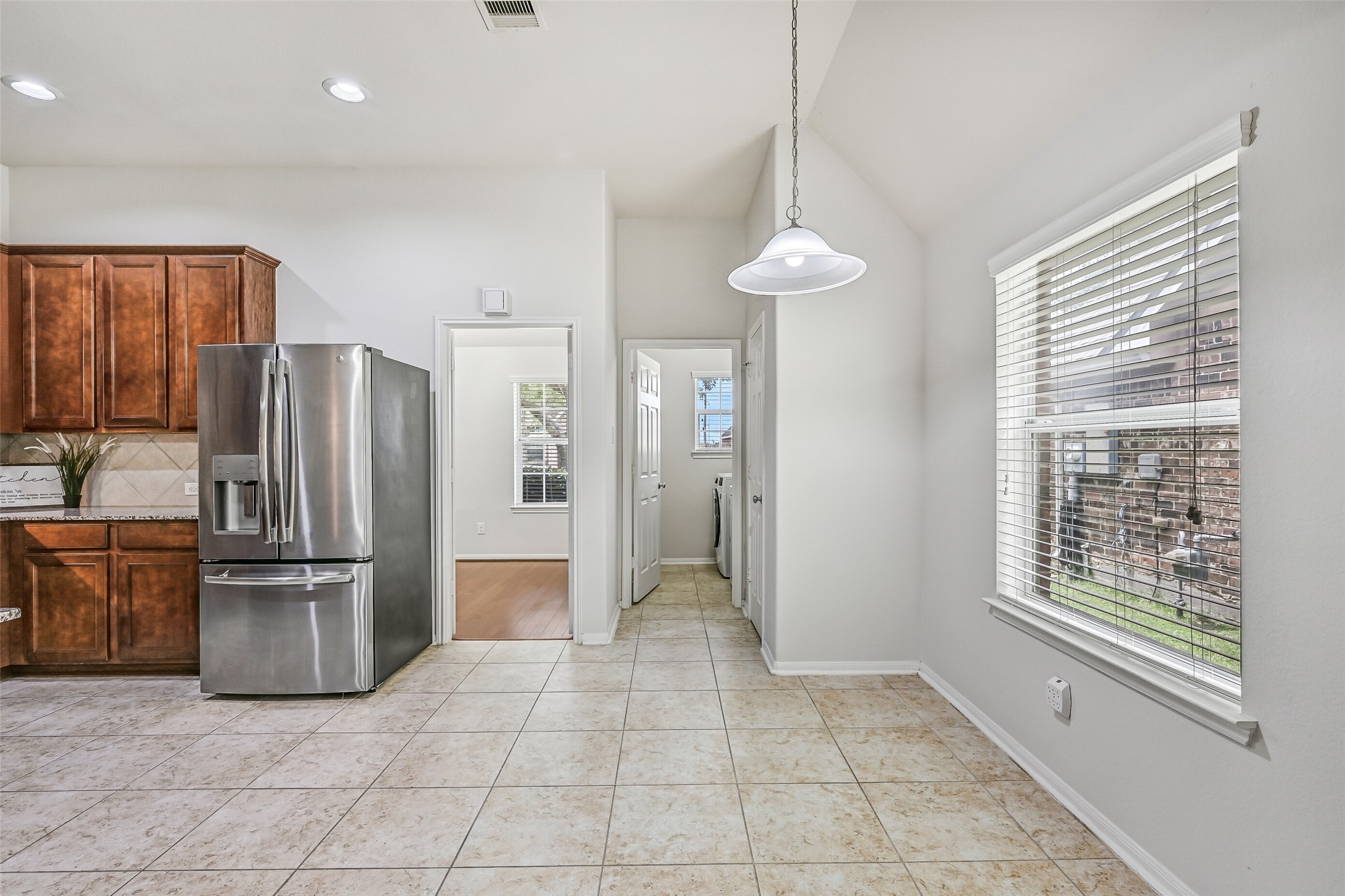 Natural light fills the breakfast area through a large window with 2" blinds, while tile flooring continues into the adjoining kitchen and utility area for a practical, easy-maintenance layout.