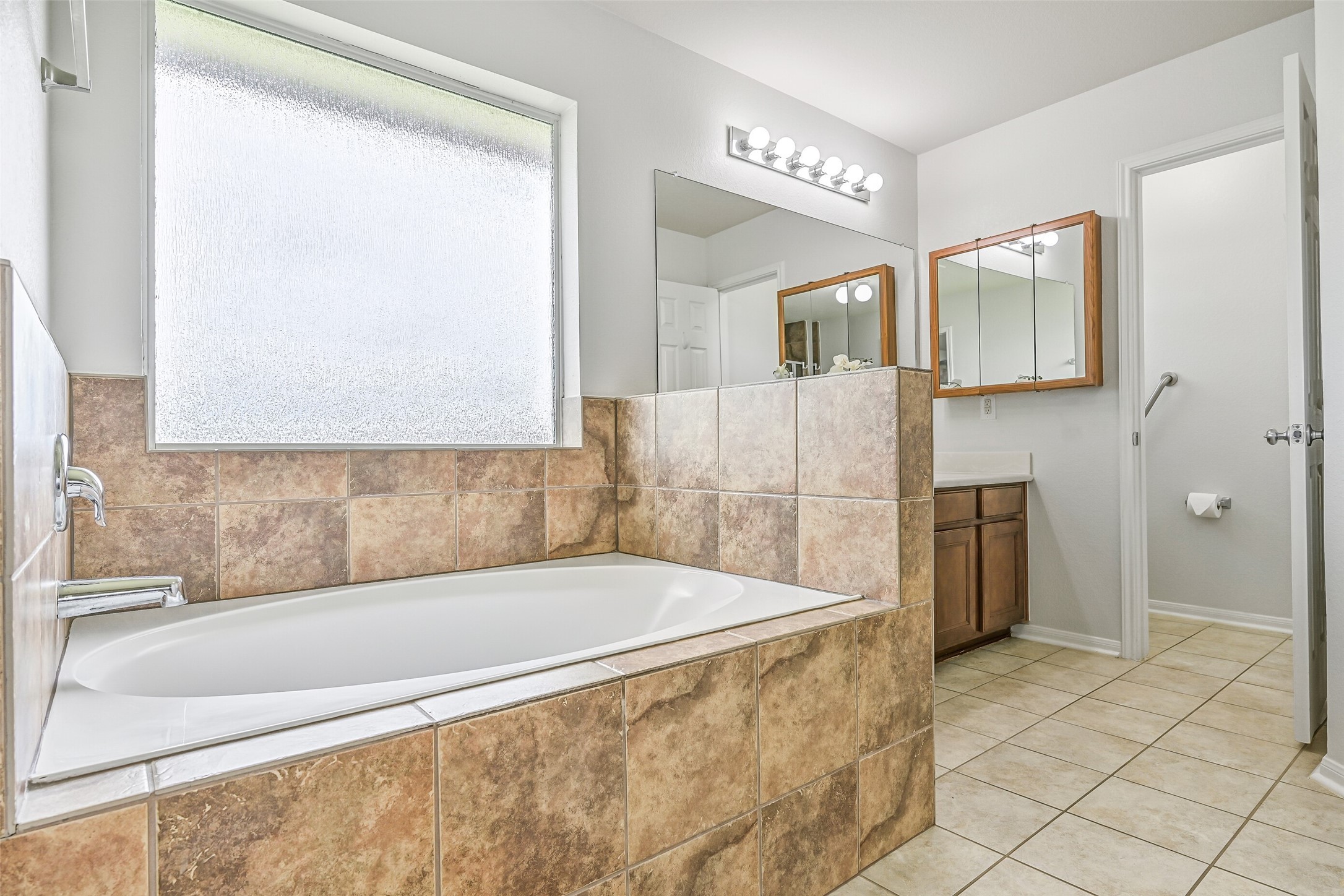 The spacious primary bath features a large tile-surround soaking tub beneath a privacy window, tile flooring and plenty of natural light, with the dual-sink vanity and separate shower completing the functional layout.