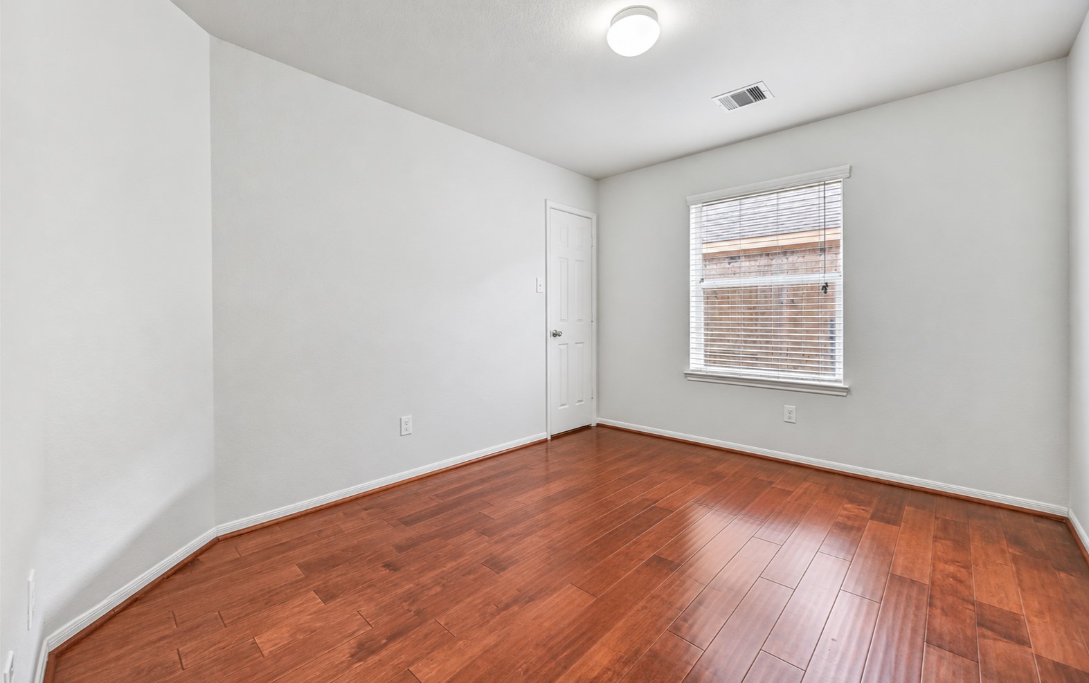 One of three secondary bedrooms offers fresh neutral paint, warm wood flooring, a large window with 2" blinds & a generous walk-in closet, continuing the home's clean, move-in ready feel.