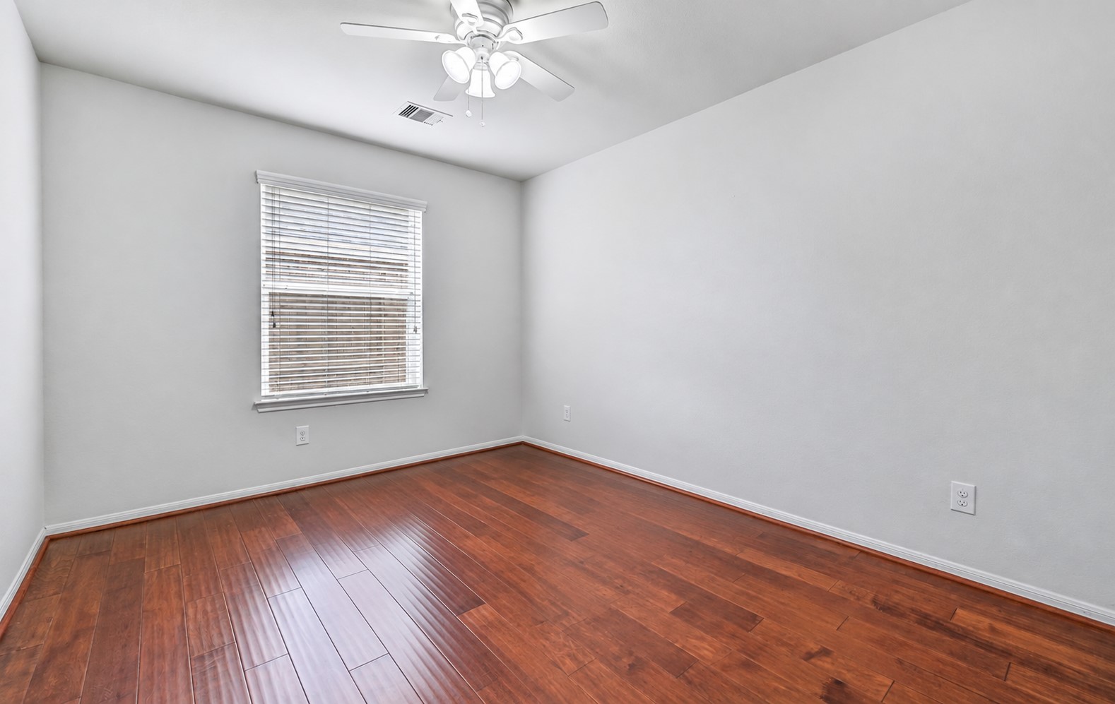 A second secondary bedroom features wood flooring, fresh neutral paint, a ceiling fan & large window with 2" blinds, offering comfortable proportions and plenty of flexibility for family, guests or hobbies.