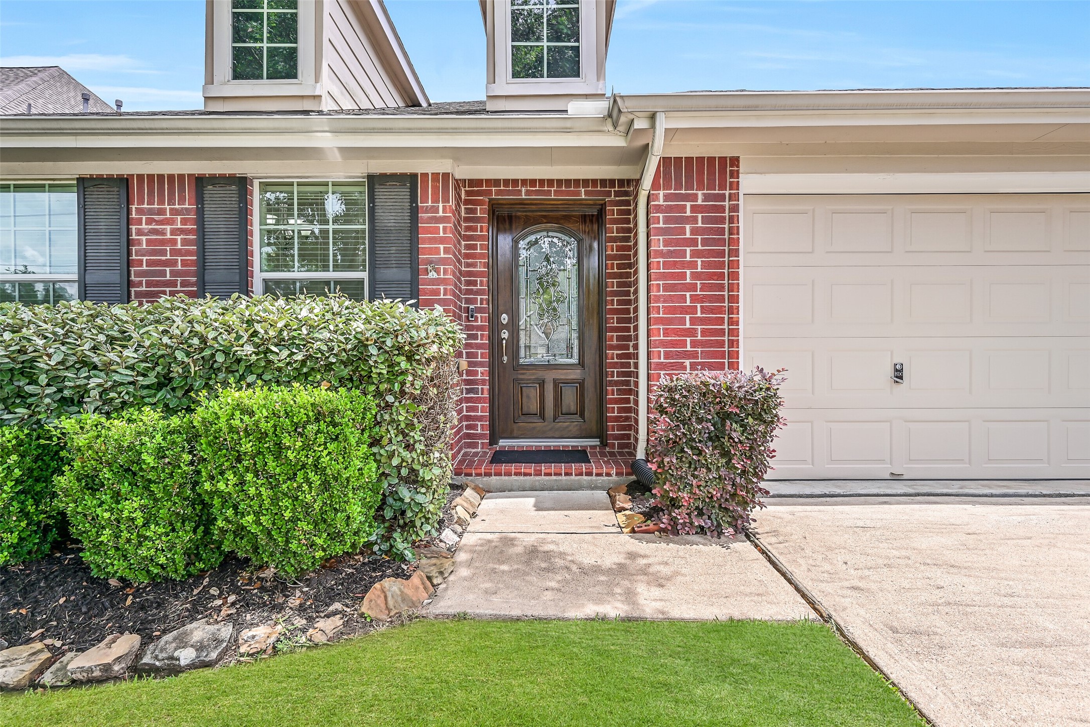 A closer look at the welcoming front entrance showcases manicured landscaping, classic brick exterior & a handsome wood front door with decorative glass, providing a beautiful introduction to this well-maintained home.