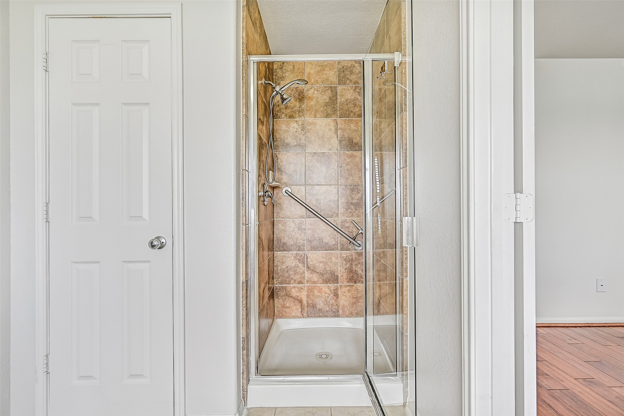 The primary bath also features a separate tile-surround shower with glass enclosure, handheld showerhead & grab bar, positioned alongside the walk-in closet for a practical and well-designed en-suite layout.