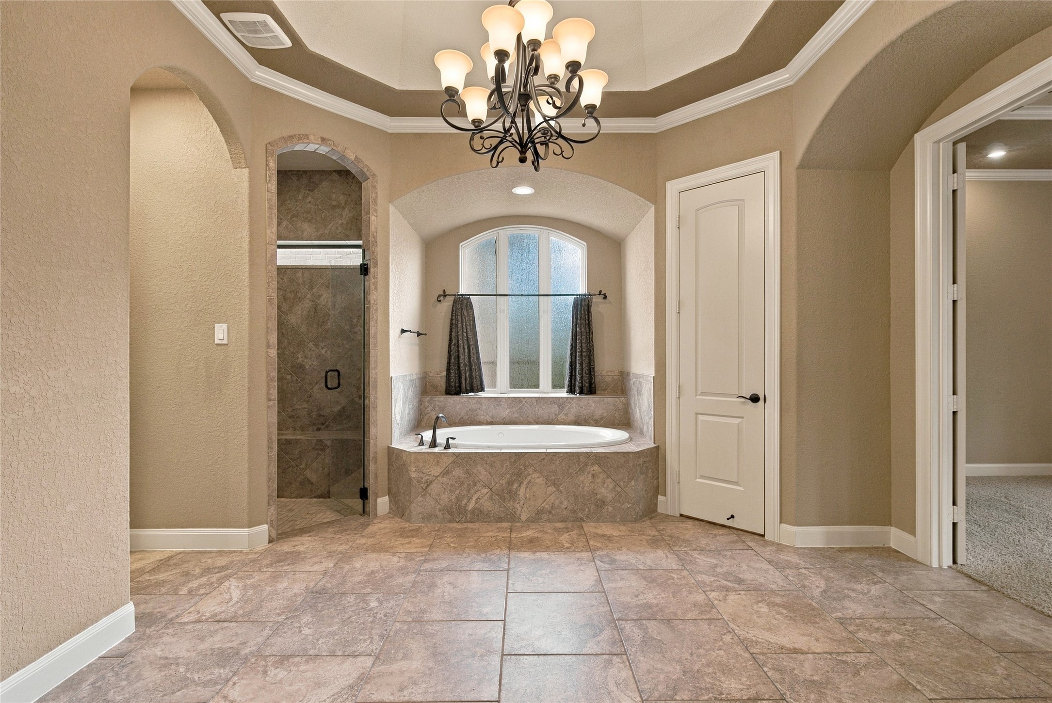 Another view of the primary bathroom showcasing the beautiful soaking tub, chandelier, and elegant architectural accents.