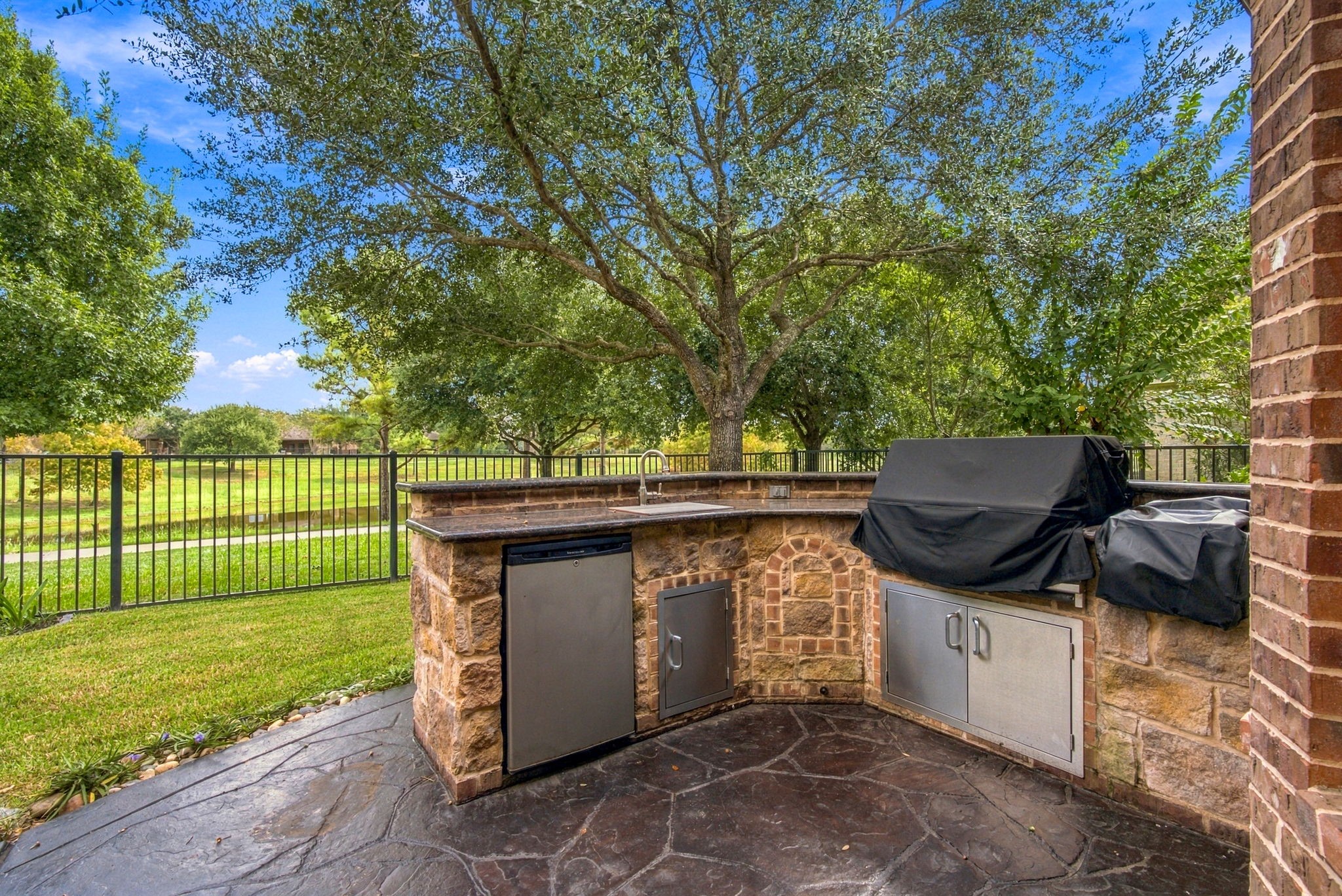 Amazing outdoor kitchen featuring stone detailing, granite countertops, a built-in grill, a sink, refrigerator, and a griddle.