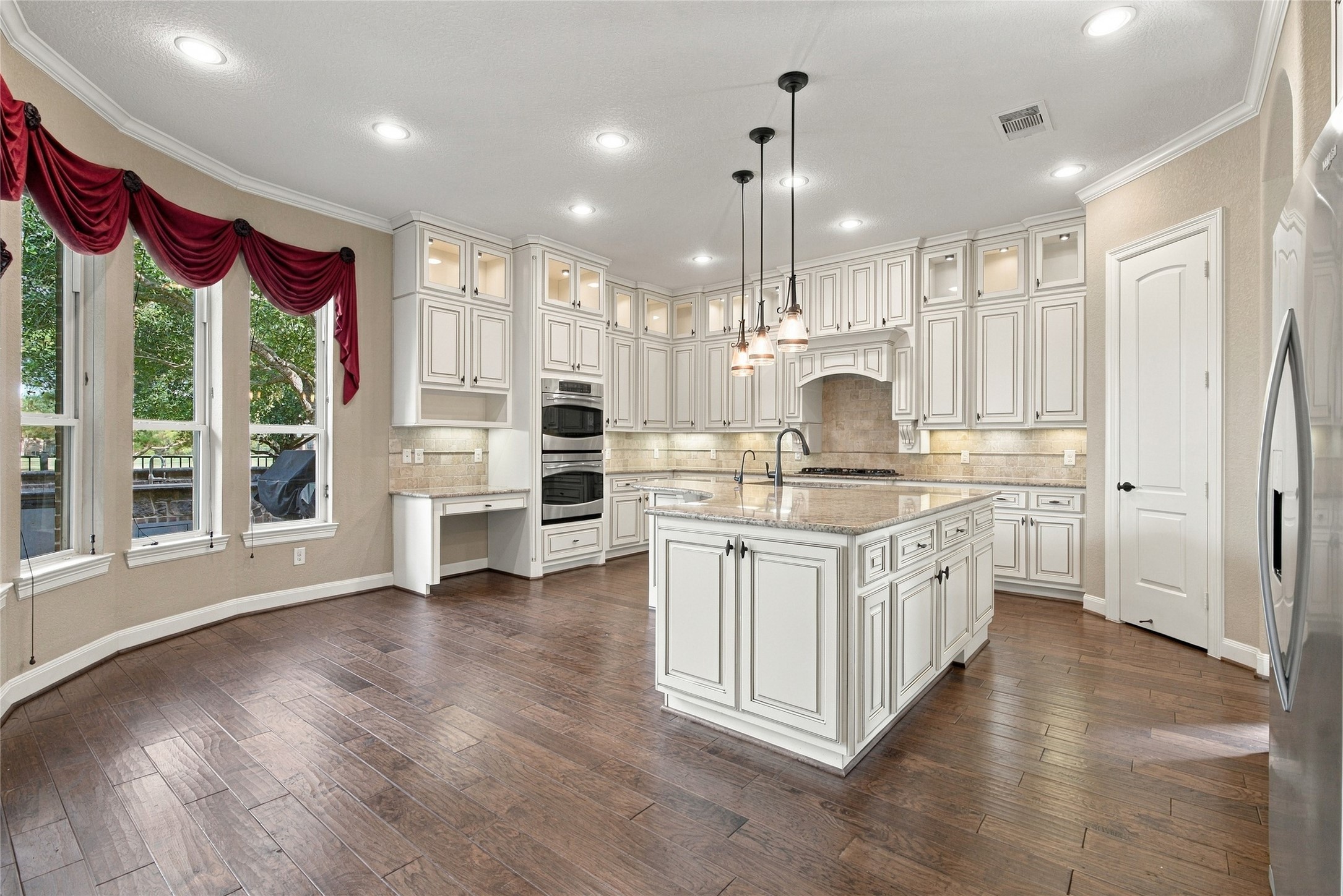 Stunning kitchen featuring granite countertops, a spacious island, cabinetry extending to the ceiling, double ovens, and beautiful wood flooring.