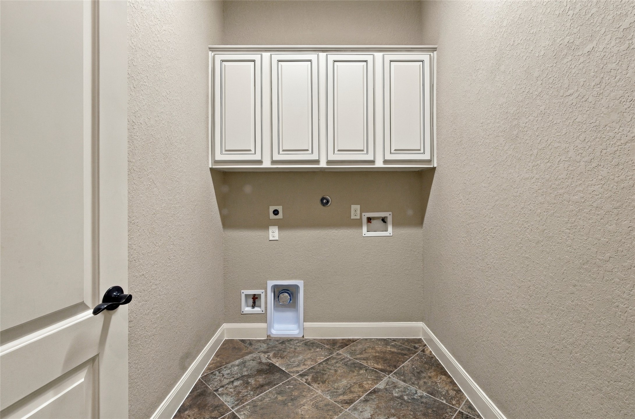 Downstairs laundry room featuring overhead cabinetry and space for a washer and dryer.