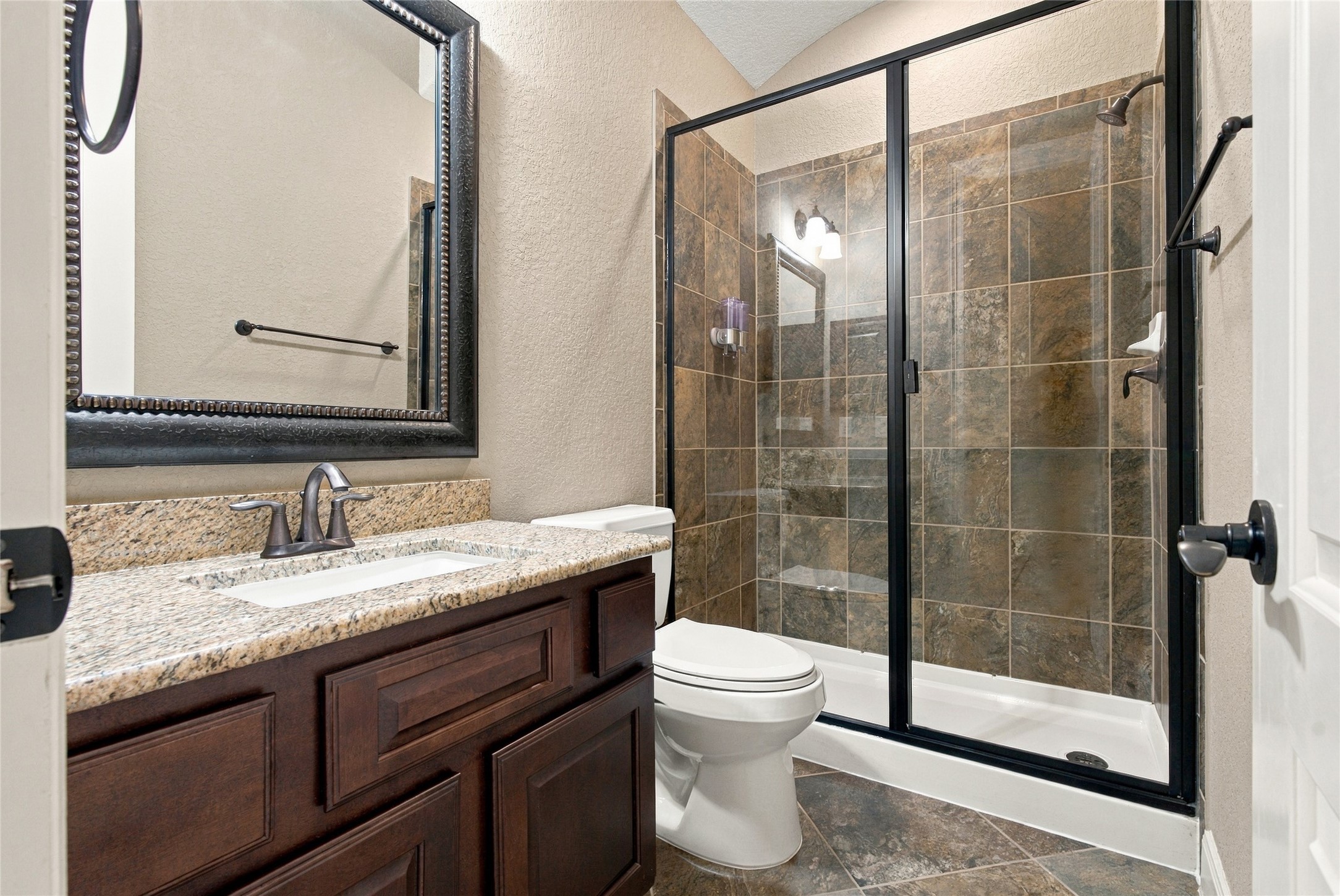 Beautifully appointed full bathroom featuring a granite countertop, framed mirror, and spacious walk-in shower with tile surround.