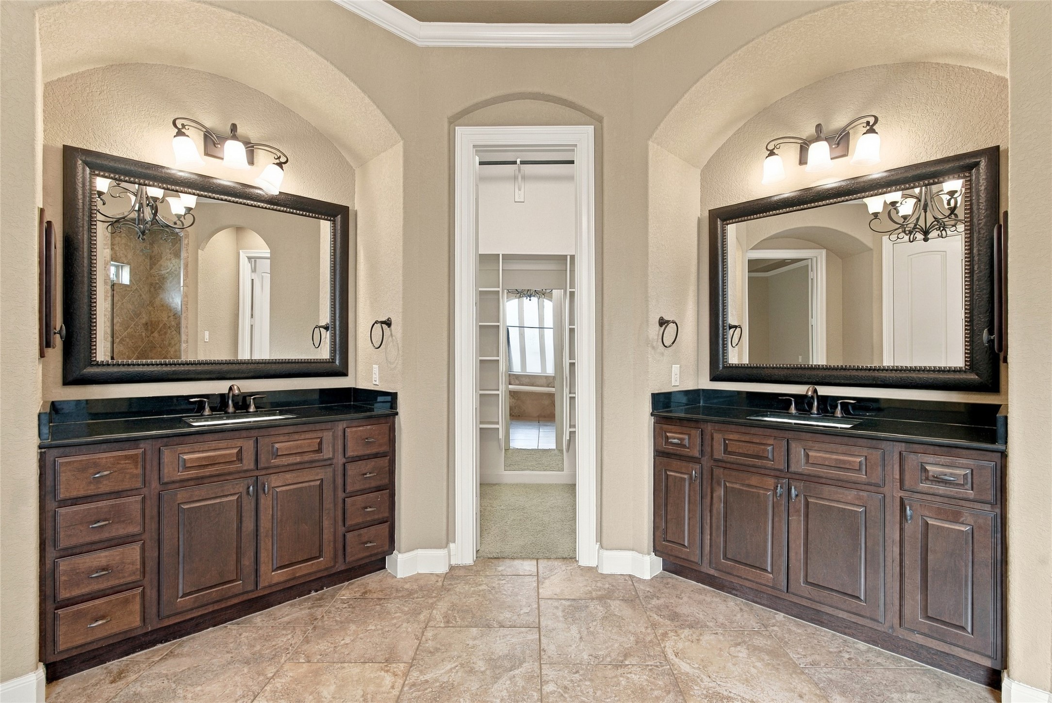 Spacious primary ensuite featuring separate granite-topped vanities, framed mirrors, and convenient access to the walk-in closets.