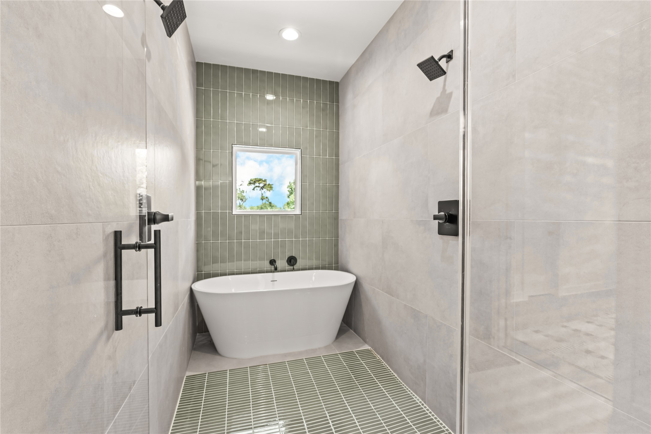 Inside view of the primary wet room/shower area featuring full wall tiling, a freestanding soaking tub nestled under a window, and a green-tiled accent floor.