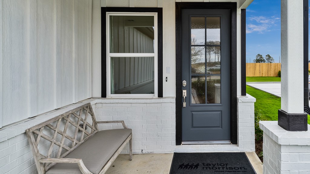 Welcoming front porch entry has crisp white vertical slat siding with brick wainscoting and a striking 6-lite custom front door in black.
