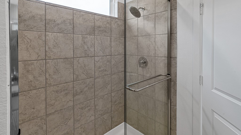 Walk-in shower has a high window and tiled walls with silver fixtures.