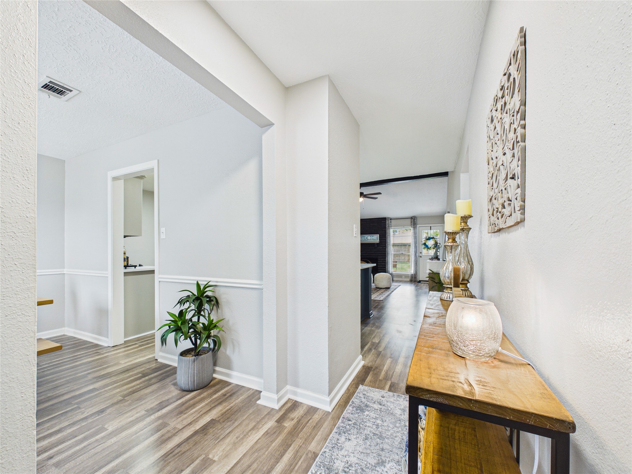 Bright and inviting hallway with elegant laminate wood flooring leads to an open living area with dining room to the left.