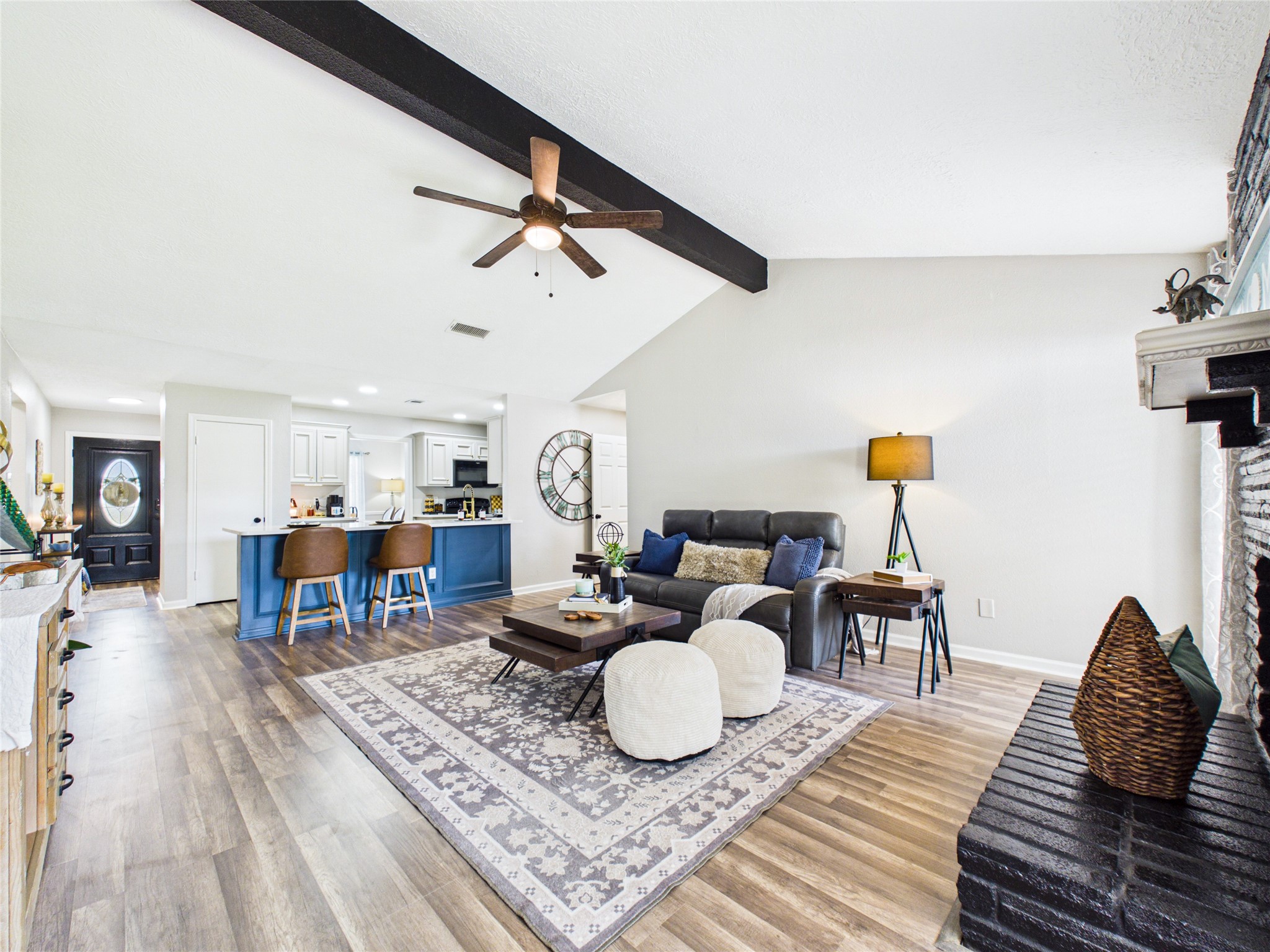 Another view of the open-concept living area with elegant wood flooring, cozy seating, and a modern kitchen featuring a breakfast bar.