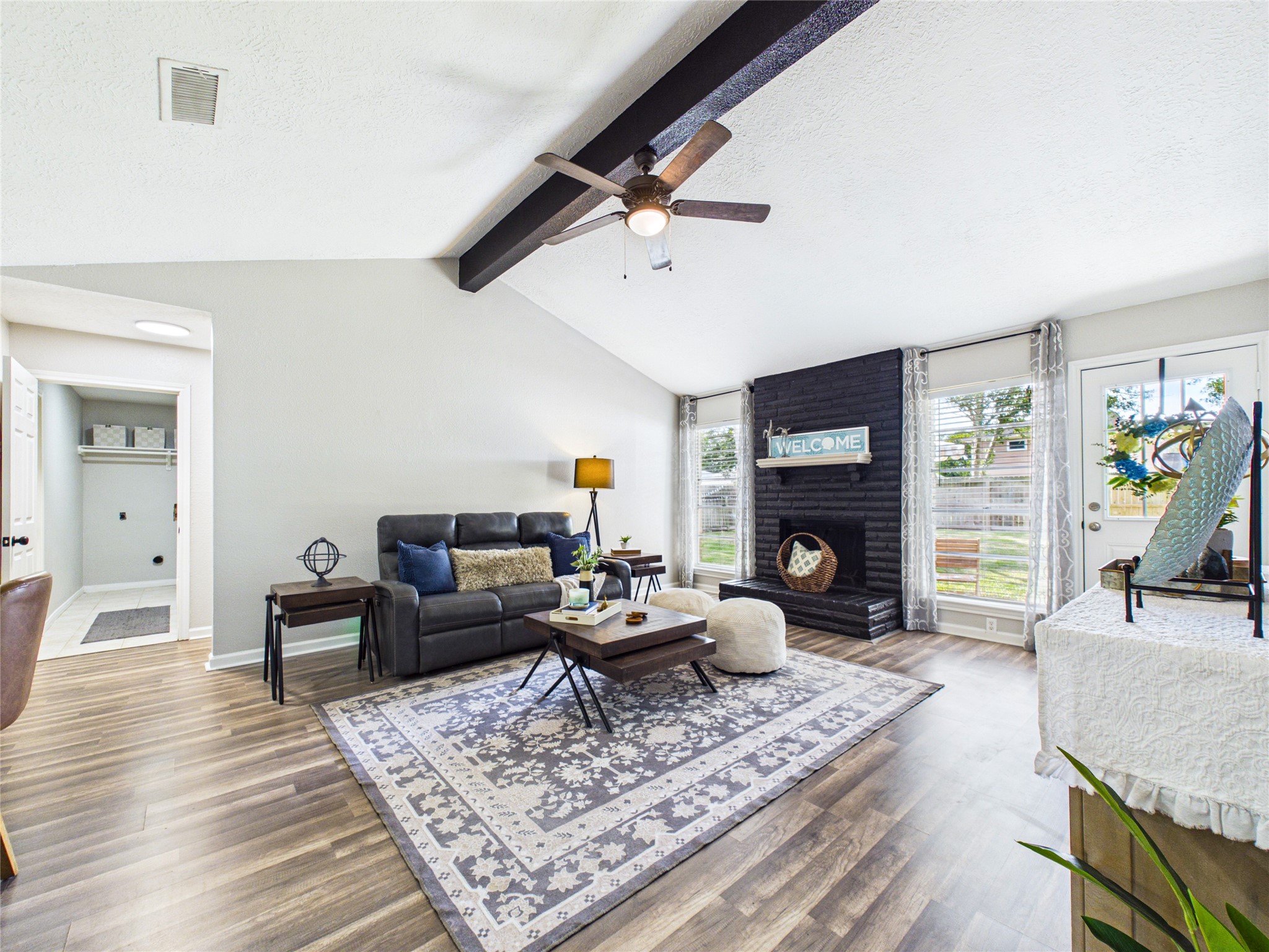 Spacious living room with vaulted ceilings, featuring a cozy black brick fireplace and ample natural light from large windows.