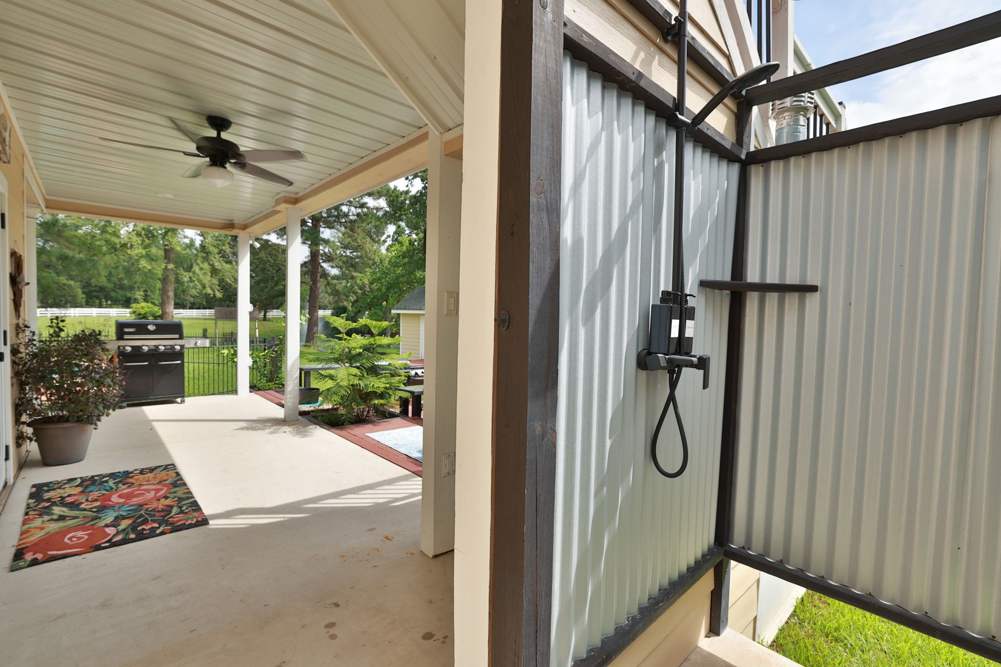 This photo shows a covered patio area with a ceiling fan and a convenient outdoor shower. Wonderful outdoor living space at it's finest!