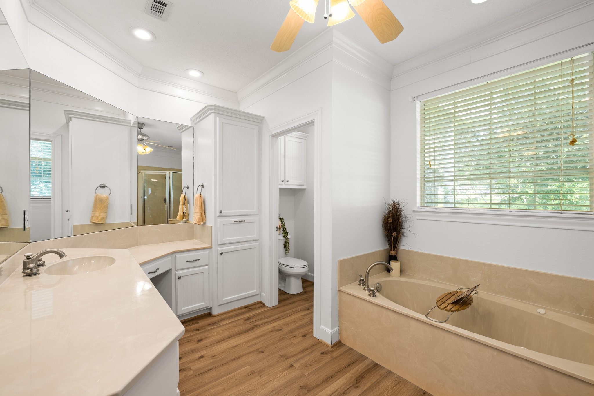 This elegant primary bathroom boasts a spacious design with a large vanity, ample storage, a relaxing tub, and warm vinyl plank flooringperfect for unwinding after a long day.