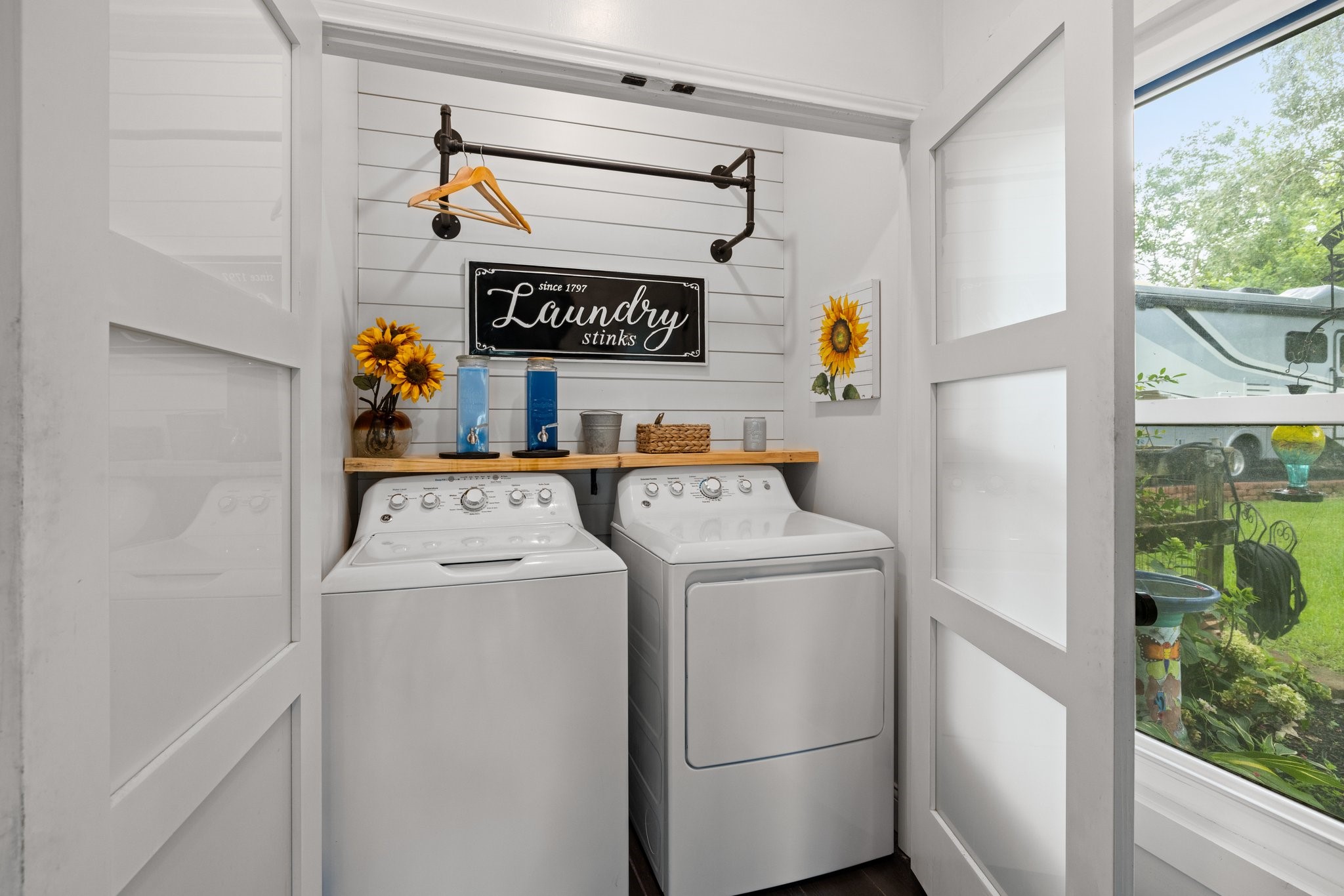 This cozy laundry room features a perfect place for your washer and dryer, decorative shelving, and an accent wall. The space is bright and functional, with charming accents like a hanging rod for a welcoming touch