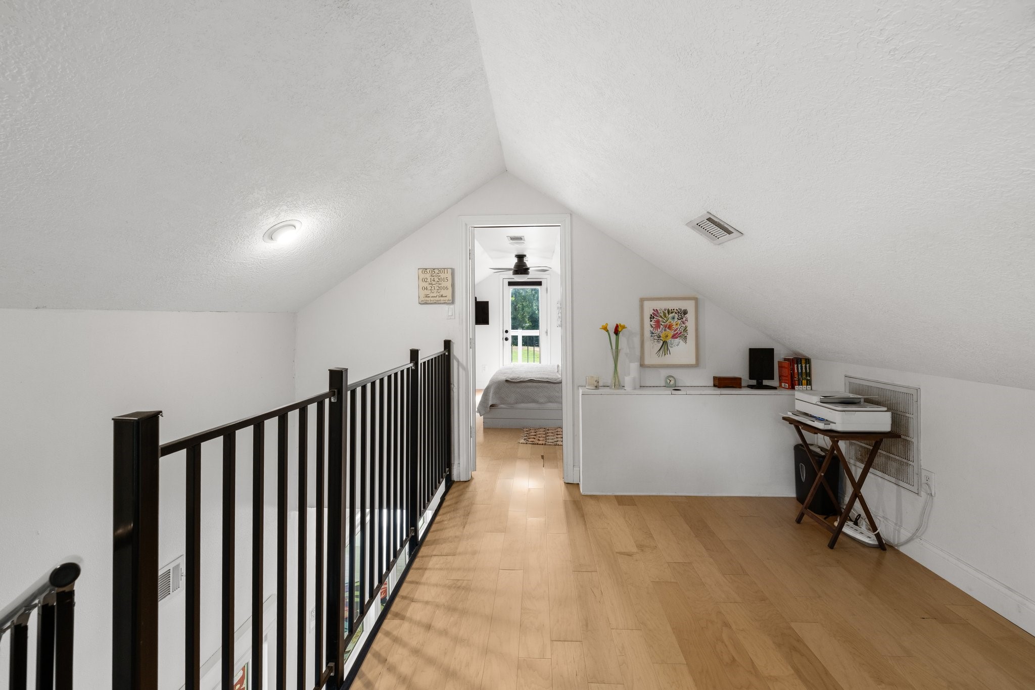 This photo showcases a loft with a sloped ceiling and wonterful flooring. It features a small railing, built-in shelf space, and leads to a cozy bedroom, creating a charming and functional upper-level space.