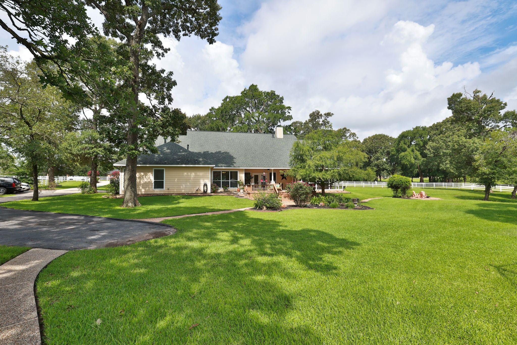 Charming home with a large, manicured lawn and mature trees. It features a spacious driveway, a welcoming porch, and is surrounded by lush greenery, perfect for privacy and outdoor activities.