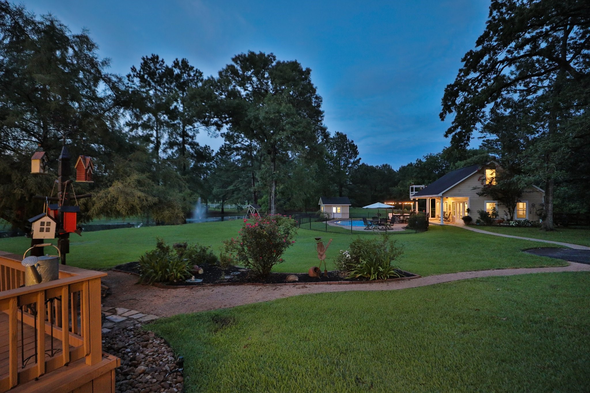 Stunning sunset view  of this serene property features a spacious backyard with lush greenery, a charming pond with a fountain, and a well-lit house. There's a pool area perfect for relaxation or entertaining. The setting feels private and inviting.