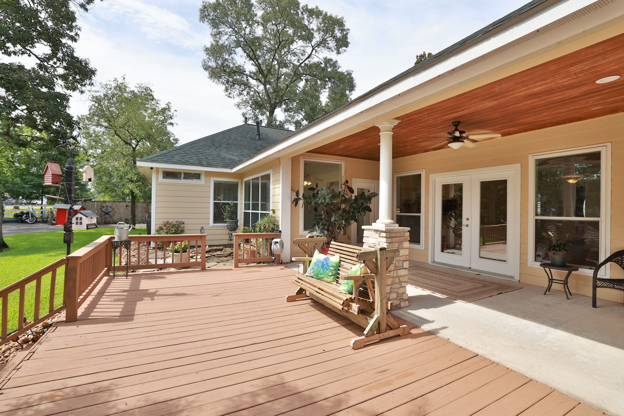 This photo showcases a spacious wooden deck with a cozy covered patio area. The patio features ceiling fans, ample seating, and large windows, offering a welcoming outdoor space with a view of the lush backyard.