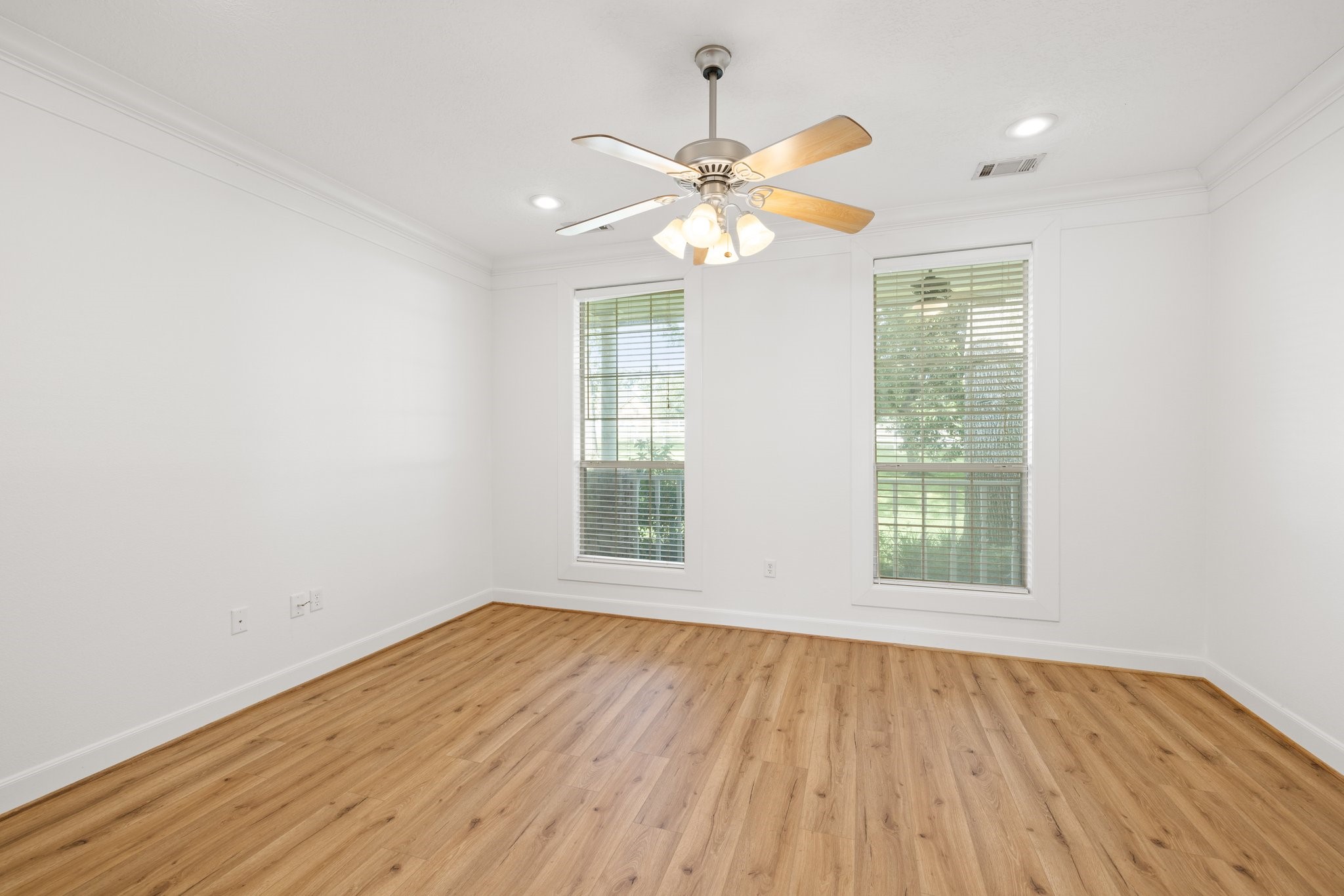 Expansive primary bedroom with elegant vinyl plank flooring, a ceiling fan, and serene outdoor views.