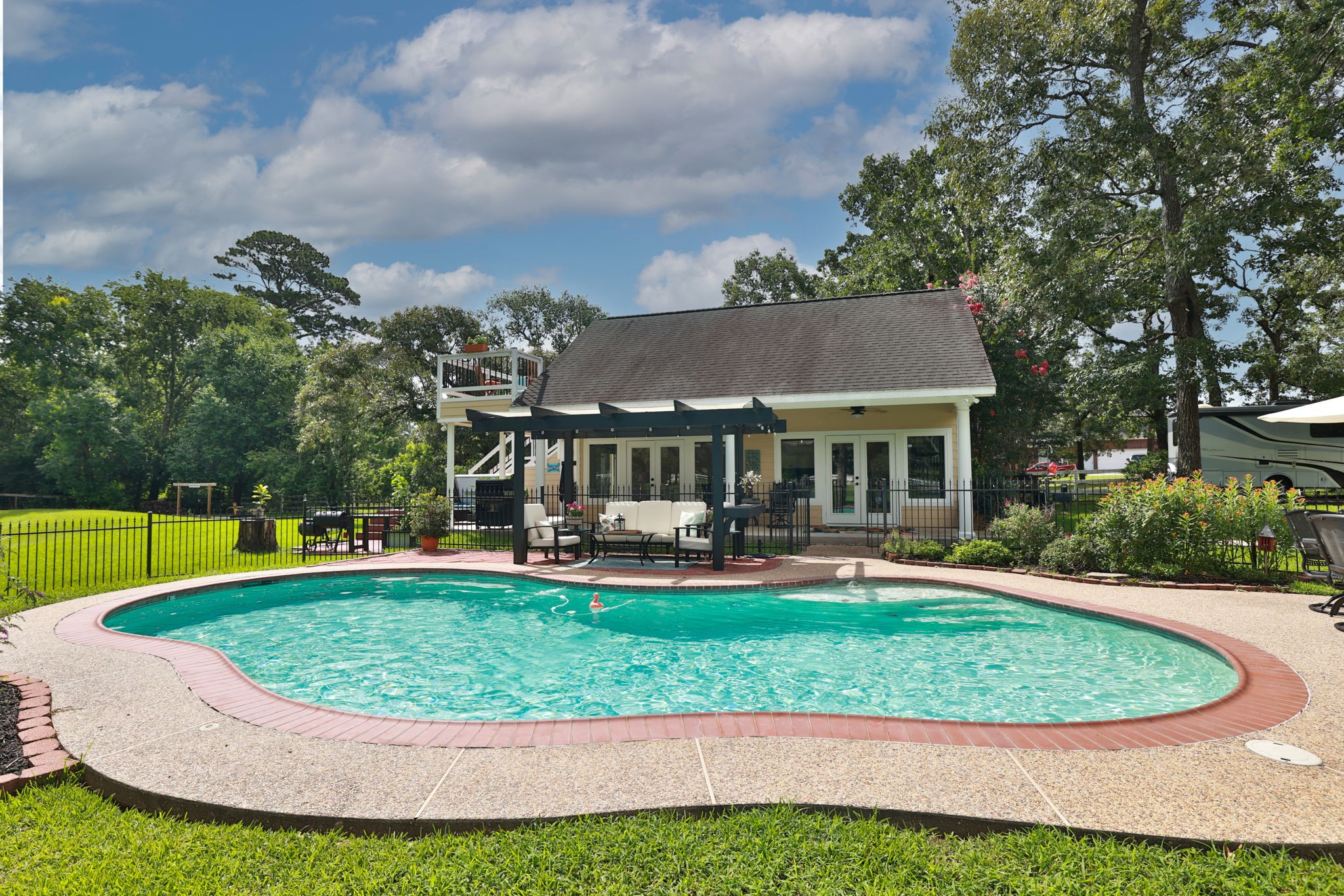 This photo showcases a charming backyard with a kidney-shaped pool, surrounded by a well-maintained lawn and a cozy patio area. The guest house has a rustic design with a pergola for outdoor relaxation, and mature trees provide shade and privacy. Ideal for summer entertaining.