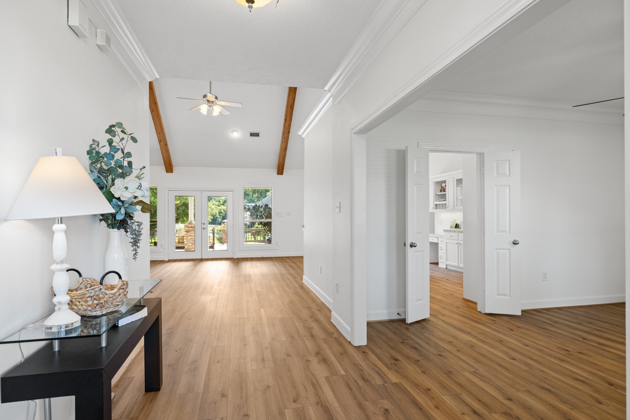 Bright and inviting entryway with vaulted ceilings and exposed beams. The open floor plan features vinyl plank flooring and leads to a spacious living area with glass doors opening to a backyard view. Bright and inviting entryway with vaulted ceilings and exposed beams. The open floor plan features vinyl plank flooring and leads to a spacious living area with glass doors opening to a backyard view.