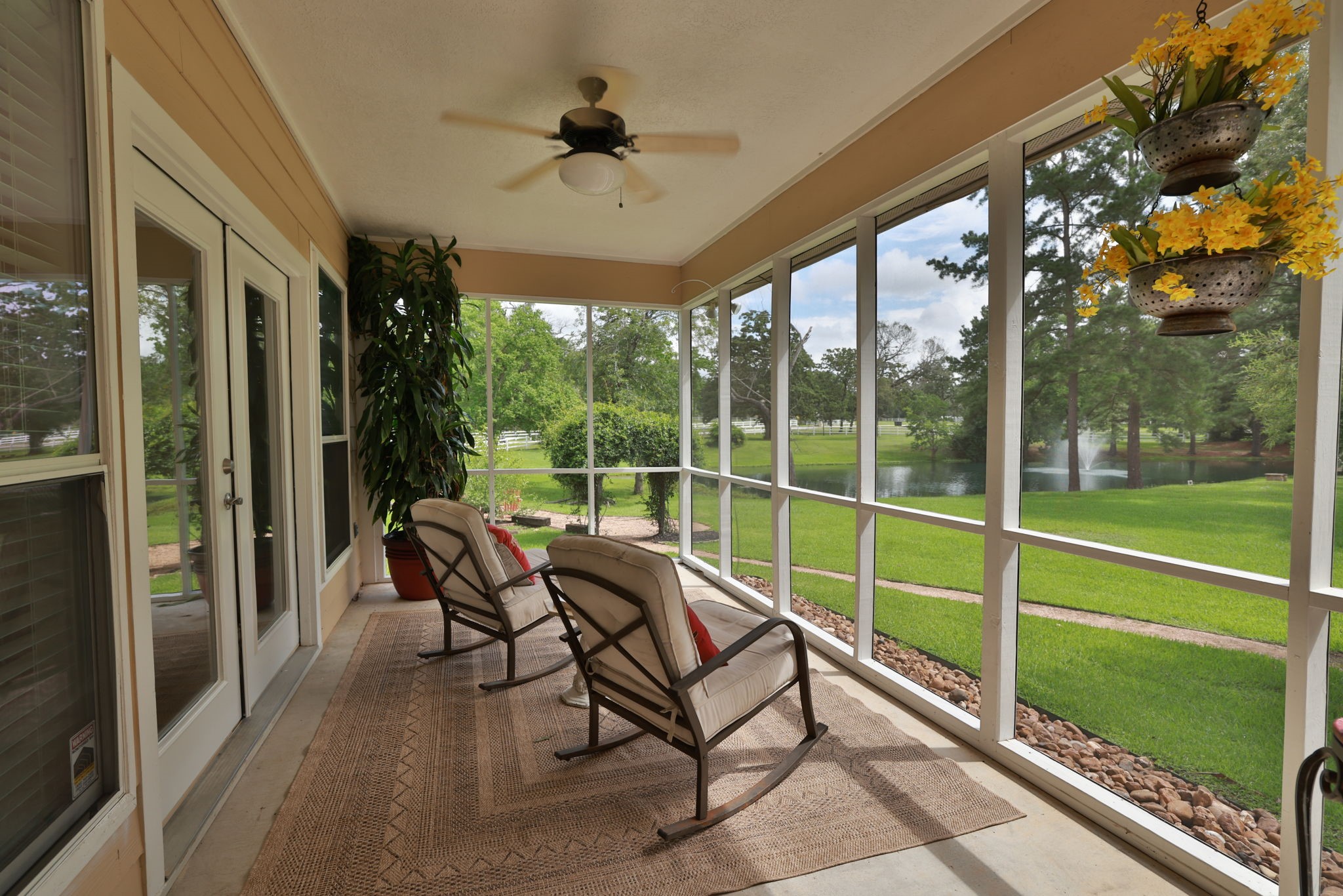 This photo showcases a serene screened-in porch room for your own cozy seating, overlooking a lush green lawn and a tranquil pond. Perfect for relaxation and enjoying nature.