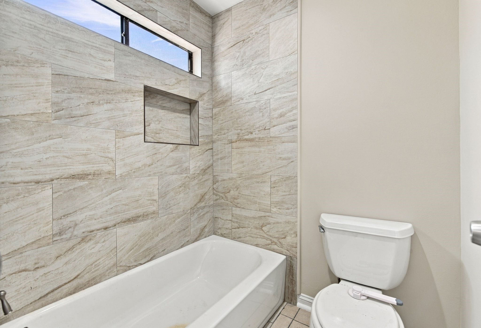 Updated tub and shower combination with contemporary tile surround and built-in niche.