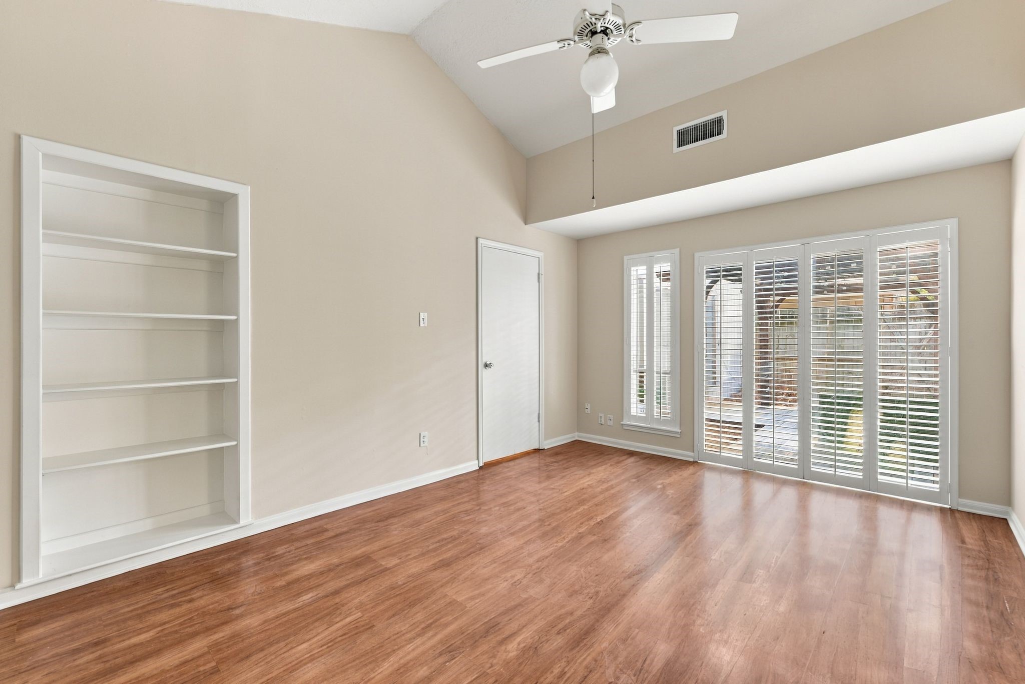 Another perspective of the primary suite showcasing the sliding glass doors, natural light, and built-in shelving.