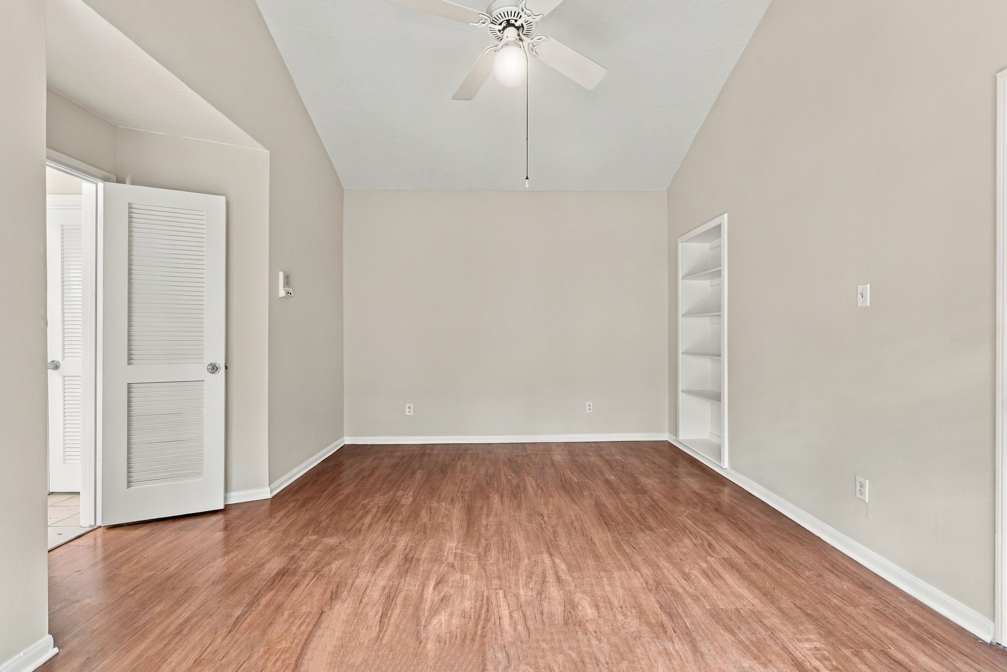 Unstaged view of the primary bedroom highlighting the vaulted ceiling, built-in shelving, and flexible furniture placement.