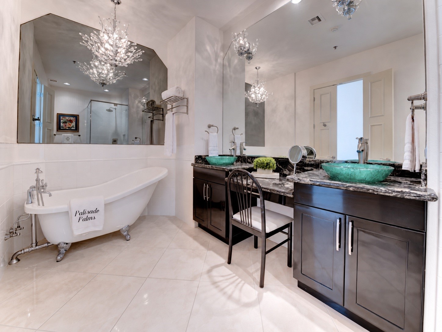 Spacious second primary bath features a claw-foot tub, dual vanities, makeup area and dramatic crystal lighting