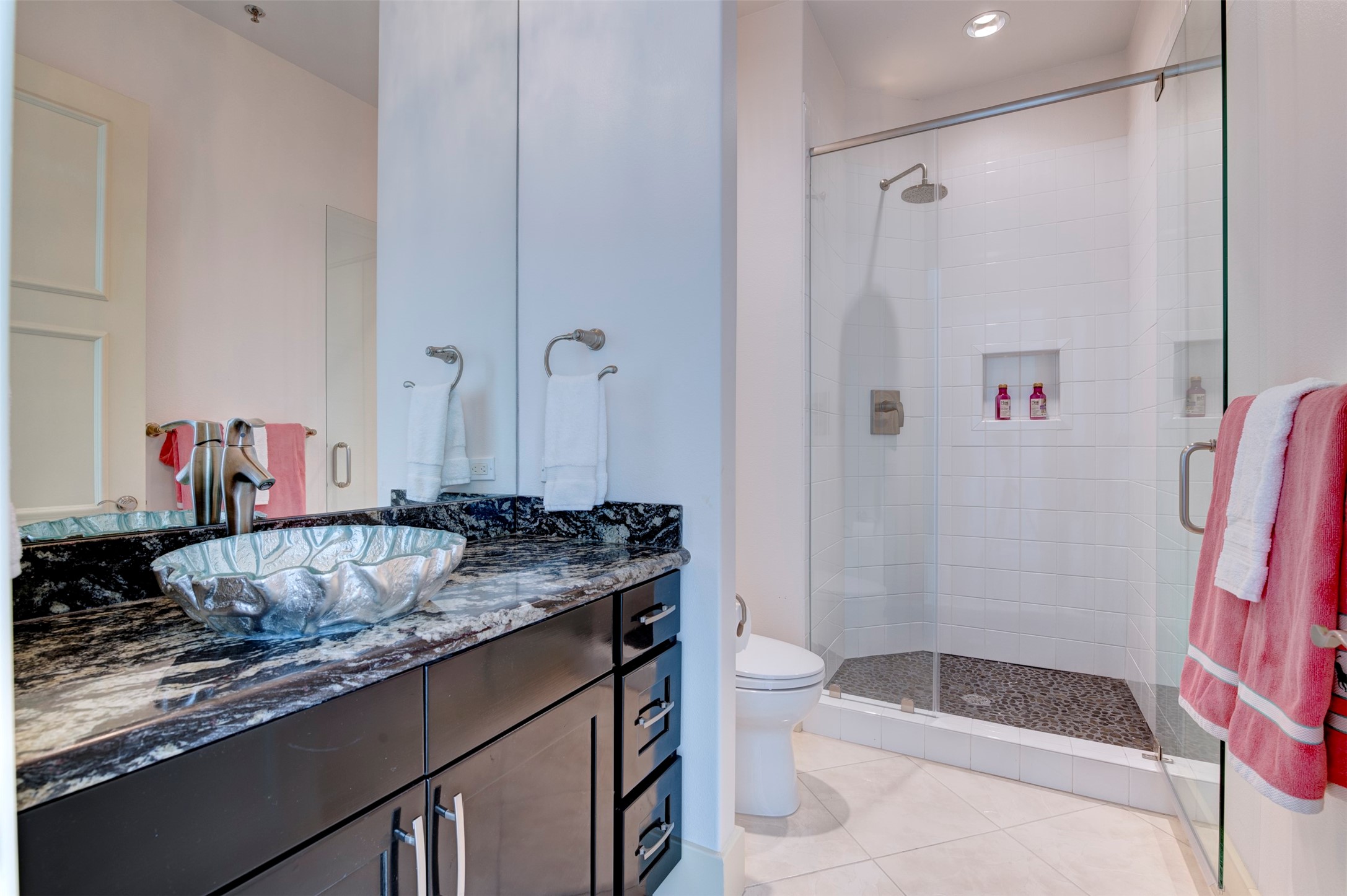 Third bath features a large glass-enclosed shower with rainfall showerhead and pebble-stone floor.