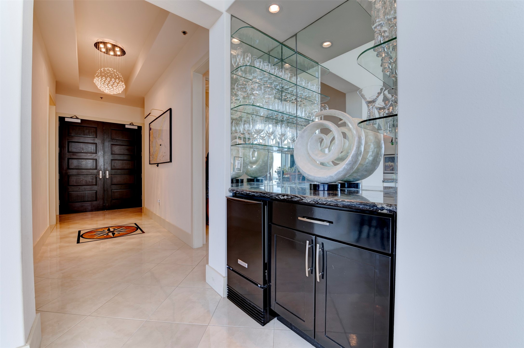 Mirrored built-in bar with extensive glassware storage and a dedicated ice maker is positioned near the entry and main entertaining areas.