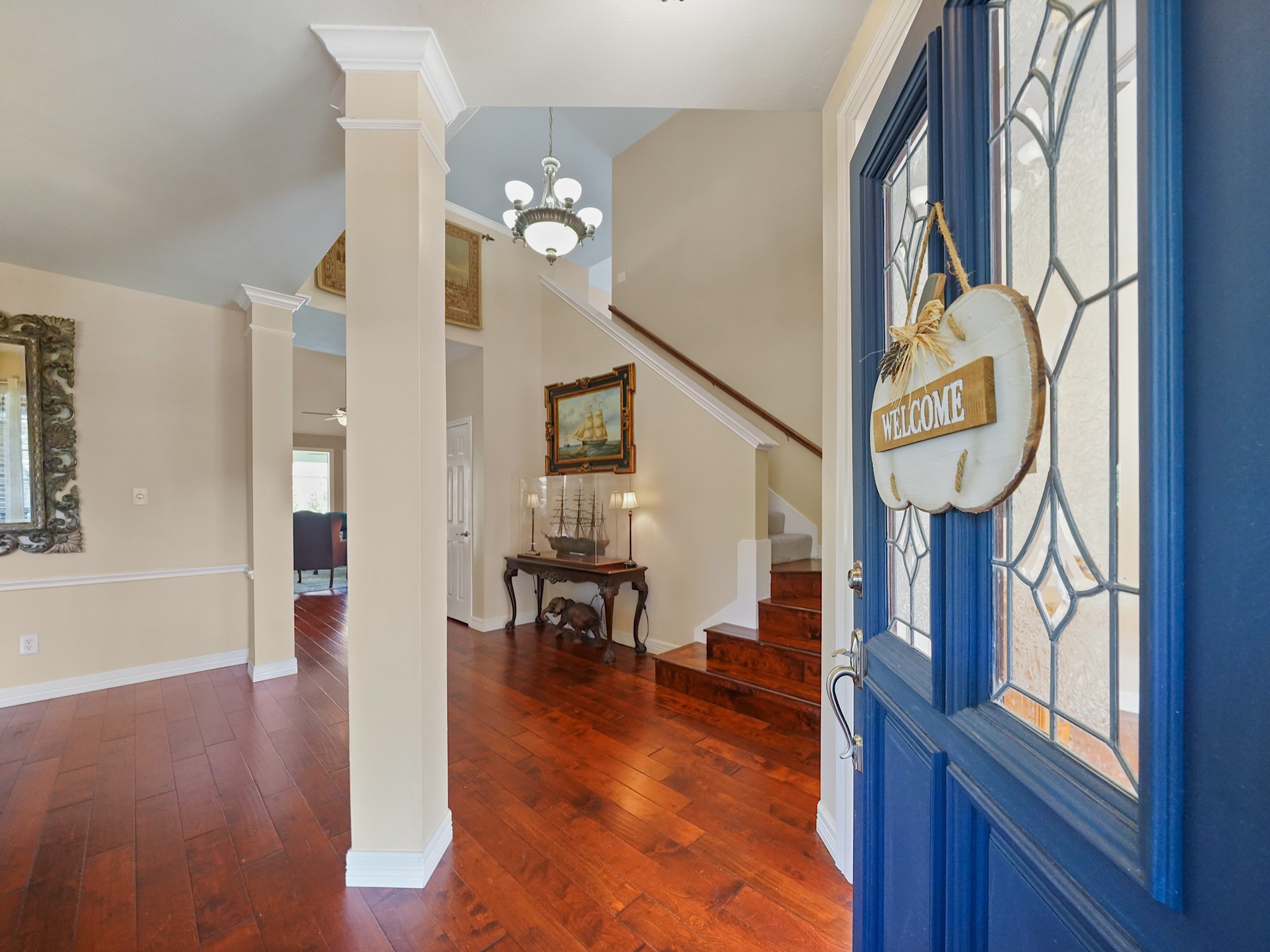 A blue front door with decorative glass welcomes you into the entry, where warm wood flooring leads toward the staircase and inviting spaces beyond. Its a charming first impression that sets the tone for the home.